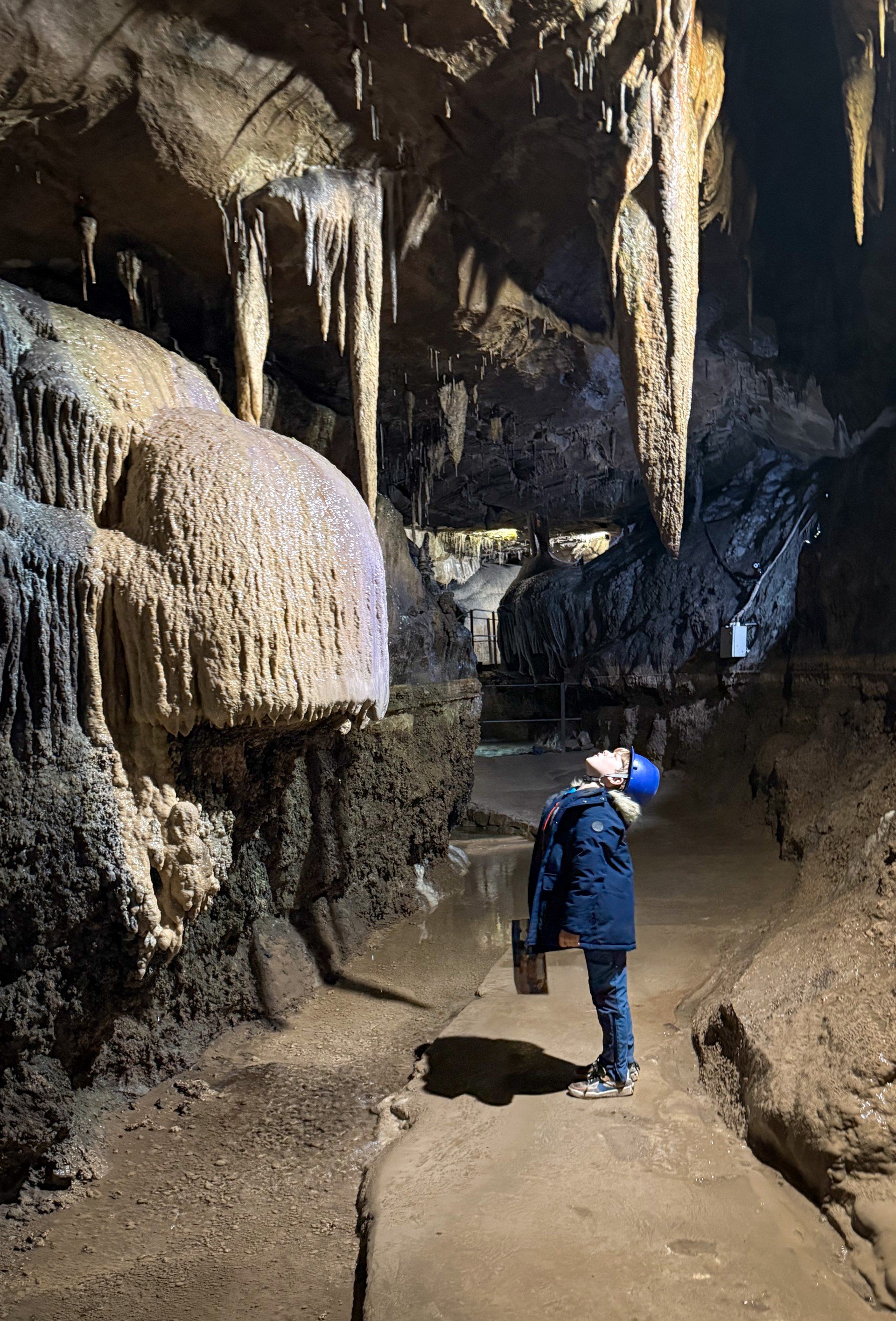 child standing in a cave in front of rock formations with a information sheet hard hat and clipboard