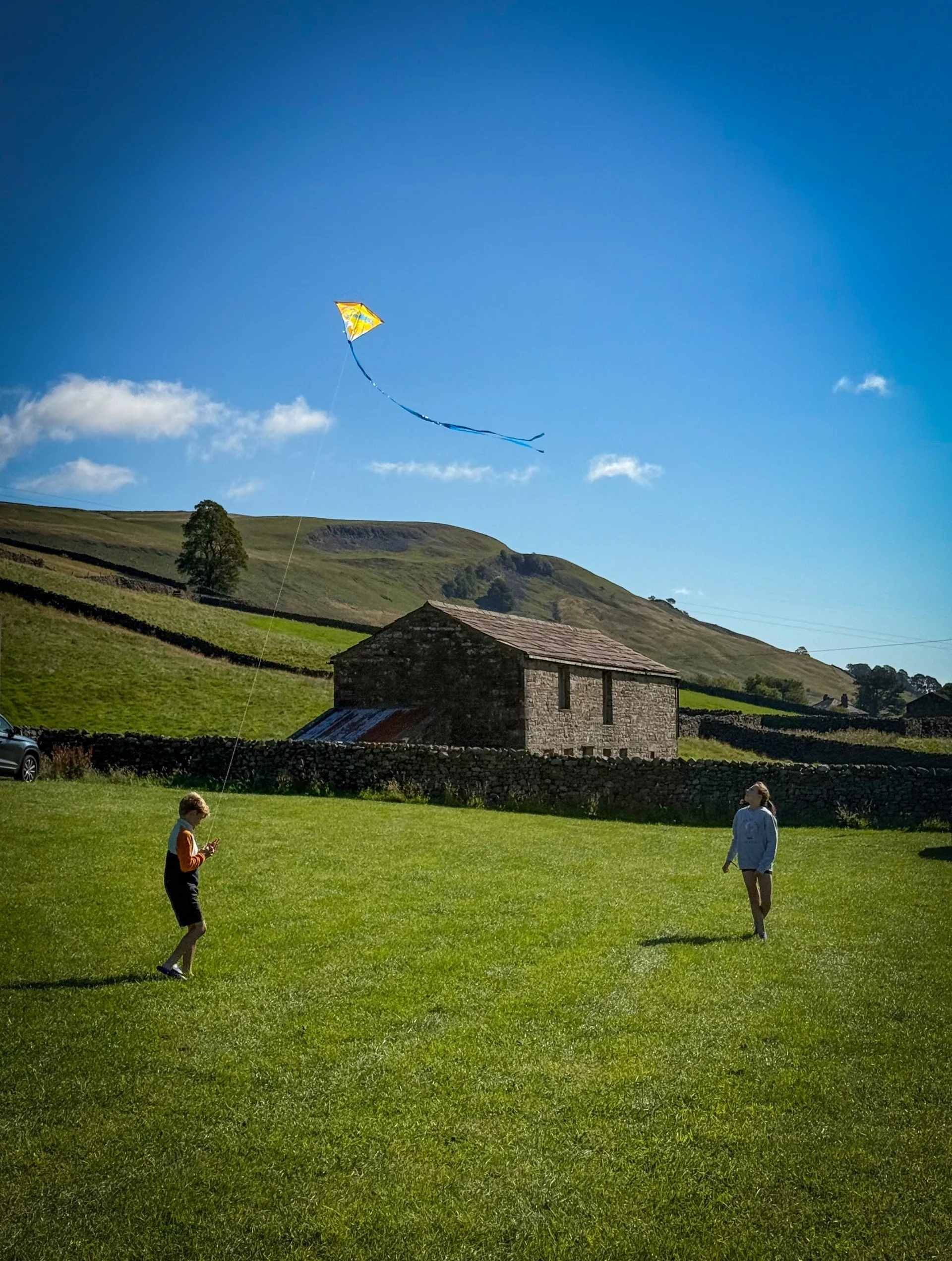 Children flying a kite in a campsite with blue skies and yorkshire dales views
