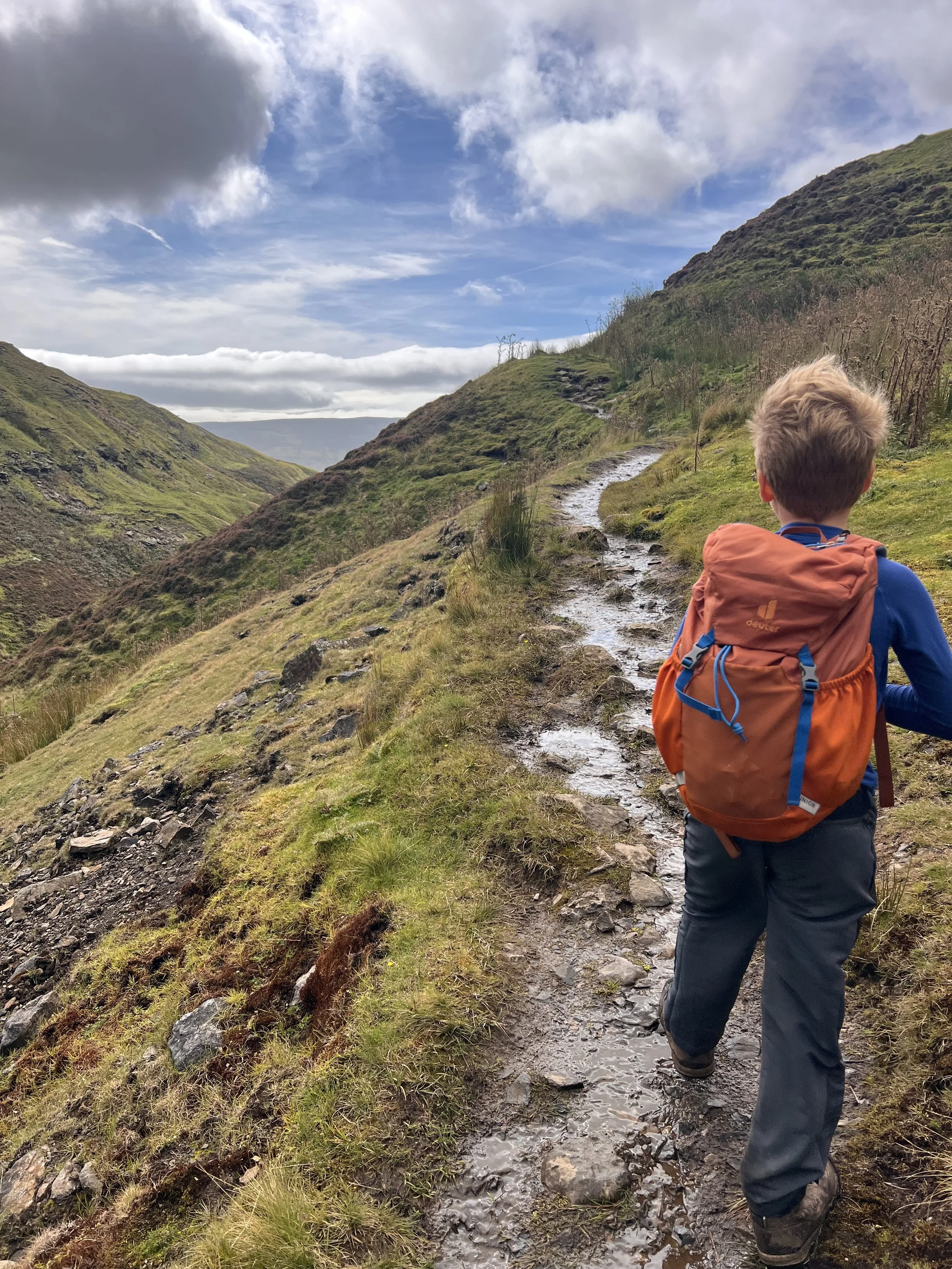 Child standing on a path with a v shaped valley to the left with blue skies