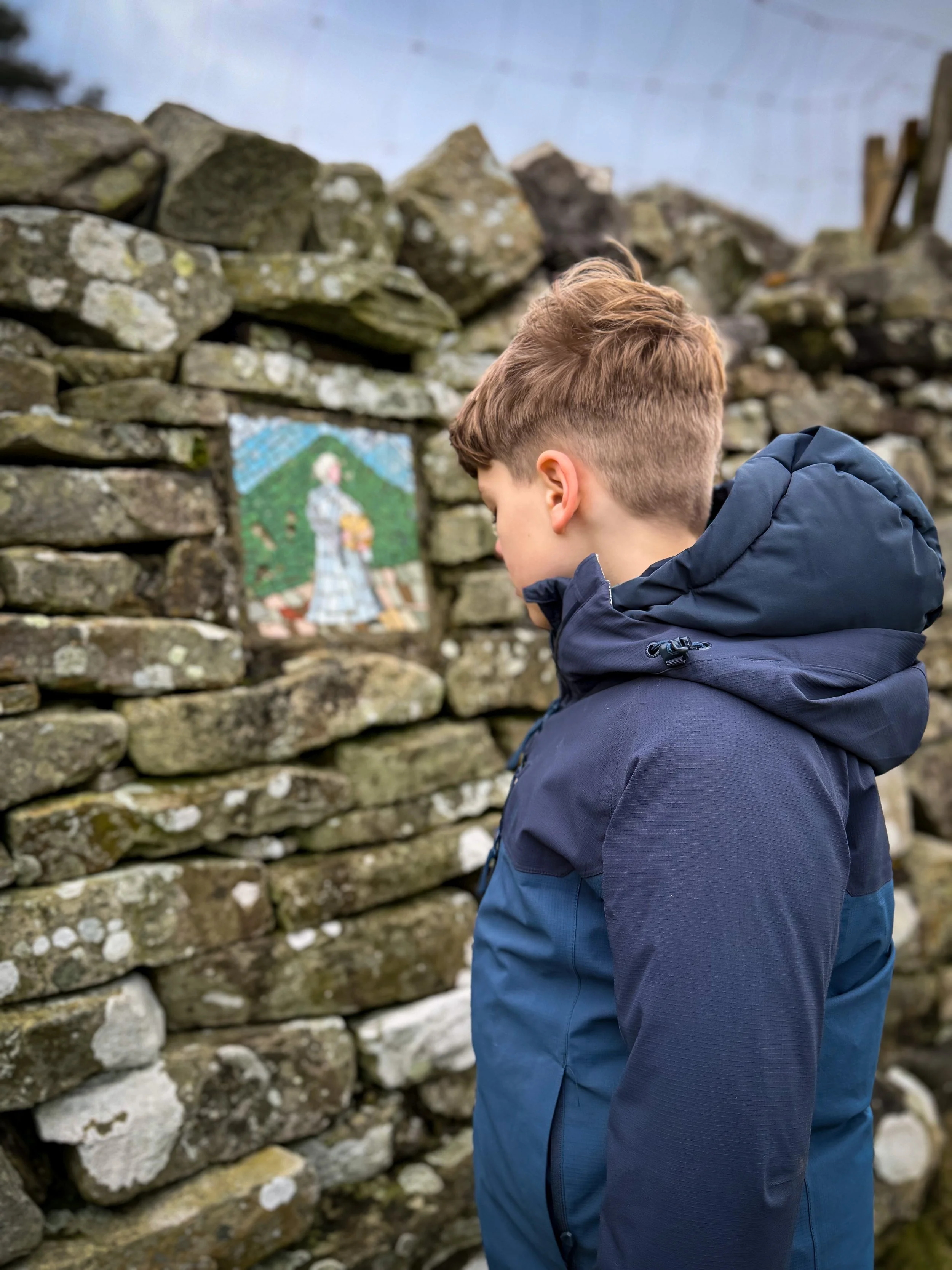Child looking at mosaic of woman in dry stone wall