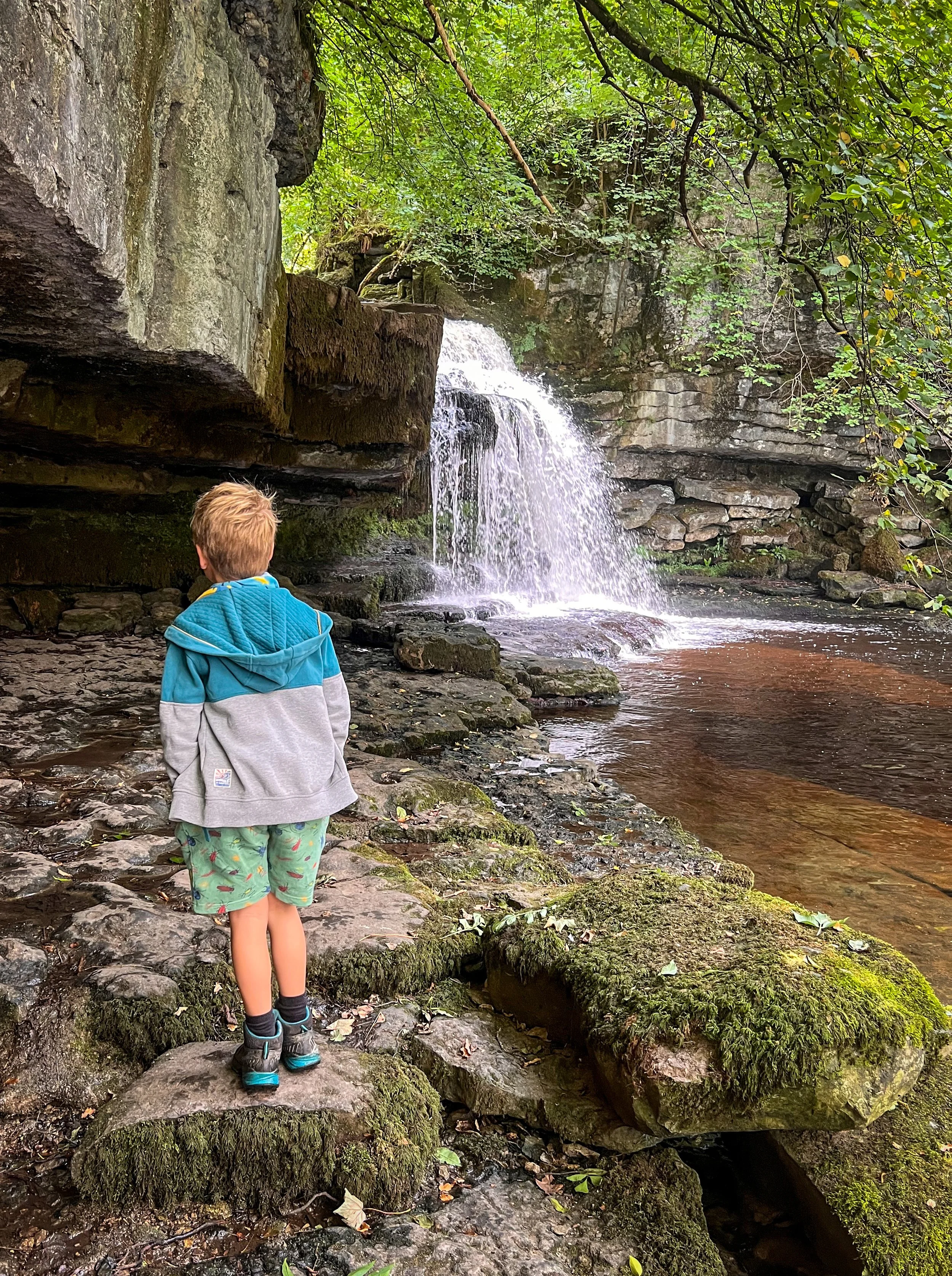Boy standing in front of a waterfall in Summer