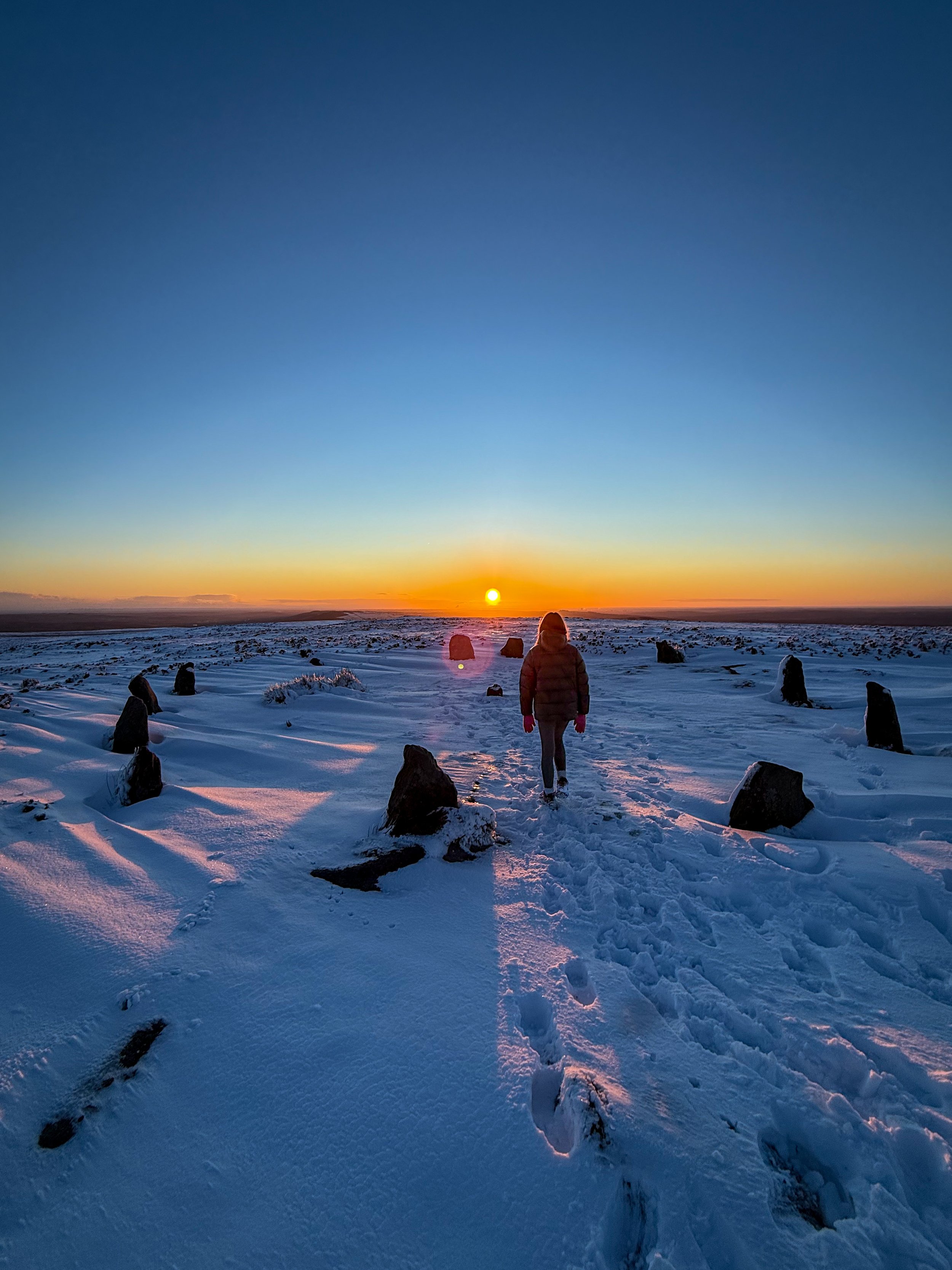 Child walking into a stone circle with snow and sunrise