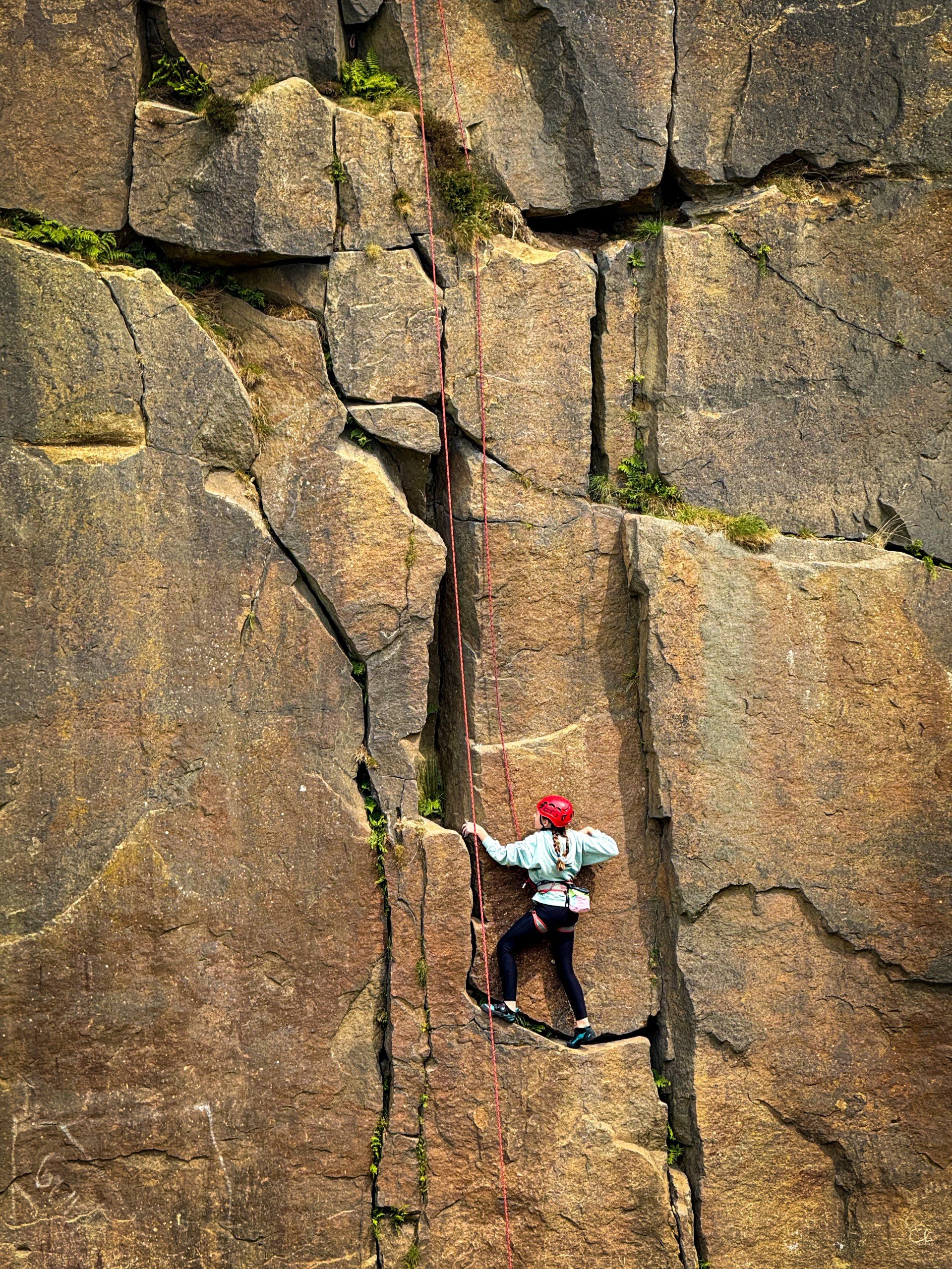Child climbing a rock face with ropes and a helmet