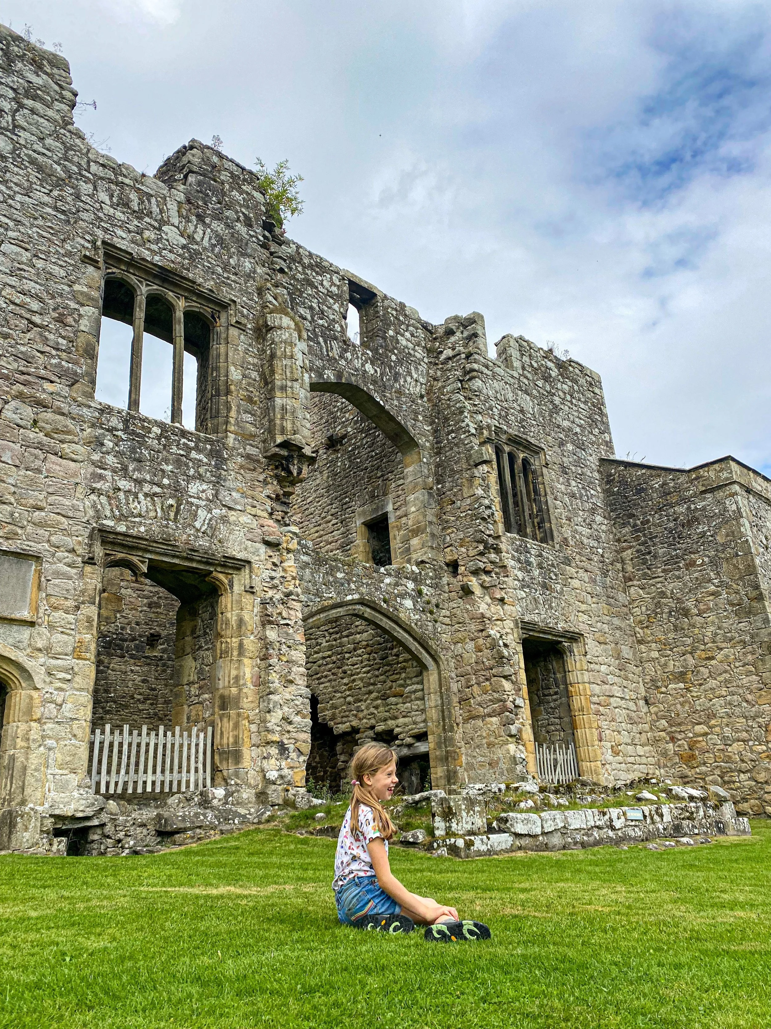 Child sitting on the grass in front of the ruins of Barden Tower