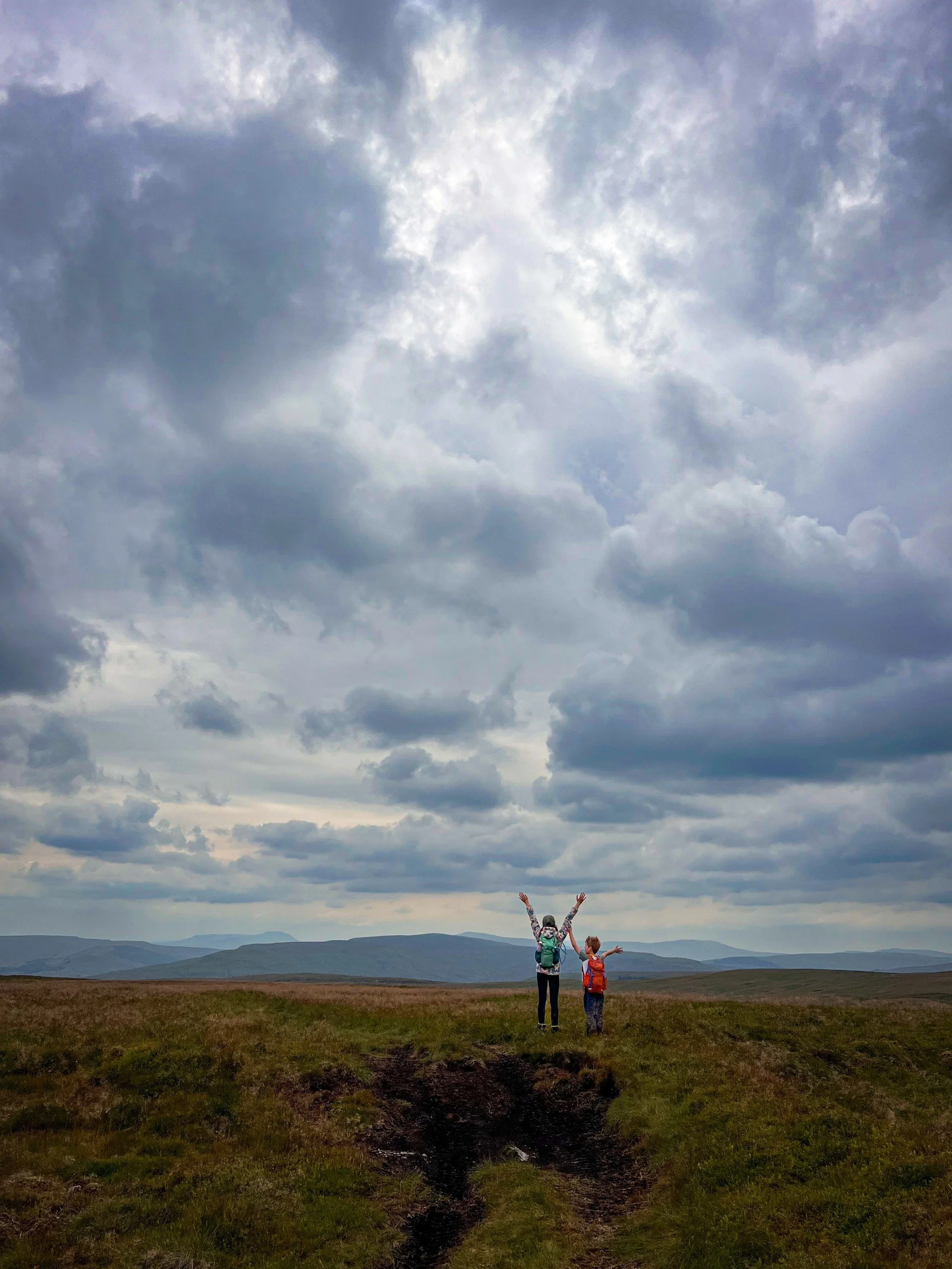 Two children on the skyline with mountains and moody grey skies above in the background