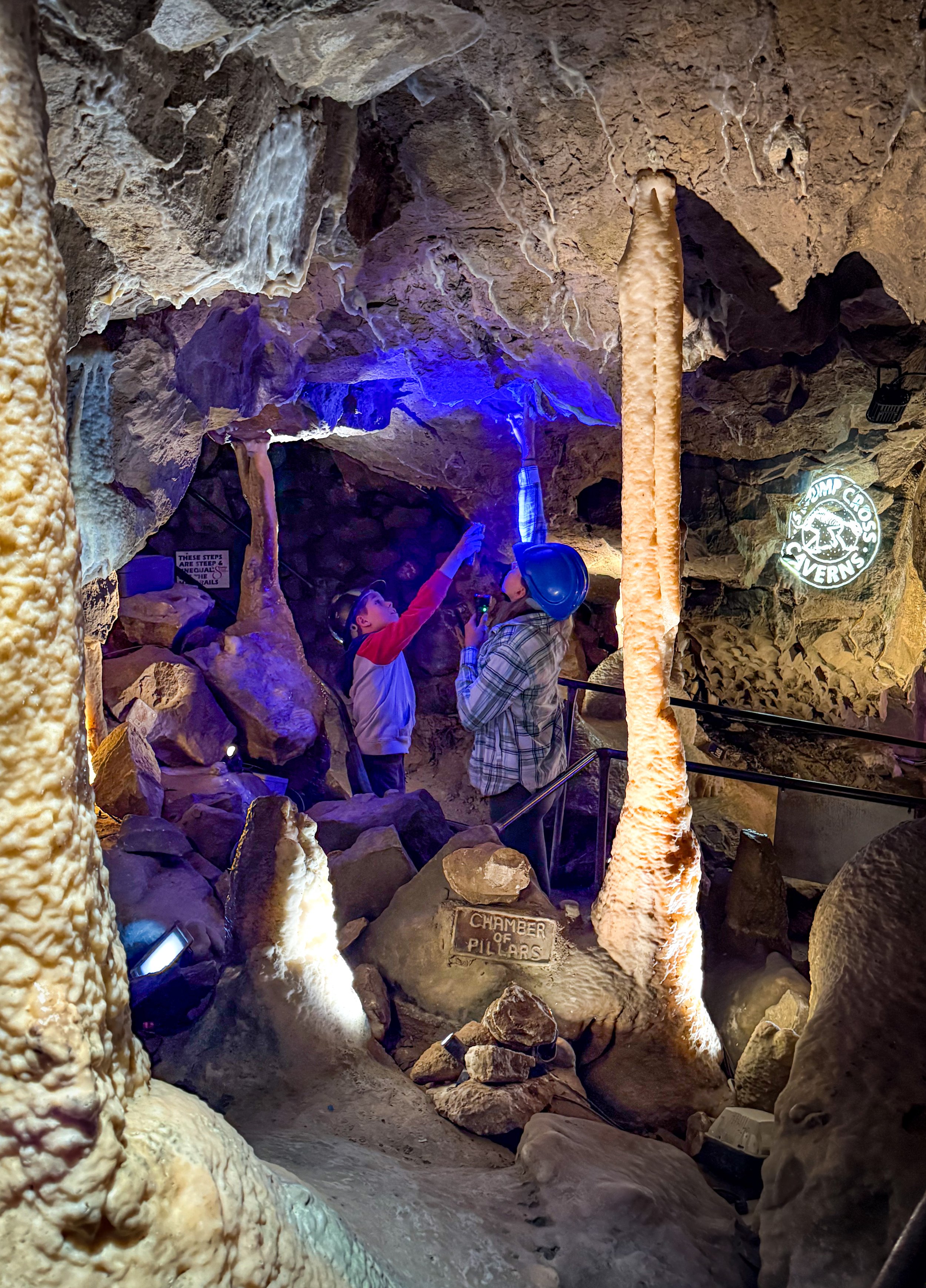 Children standing in a cavern which is lit up with purple and orange looking upwards at the roof of the cave