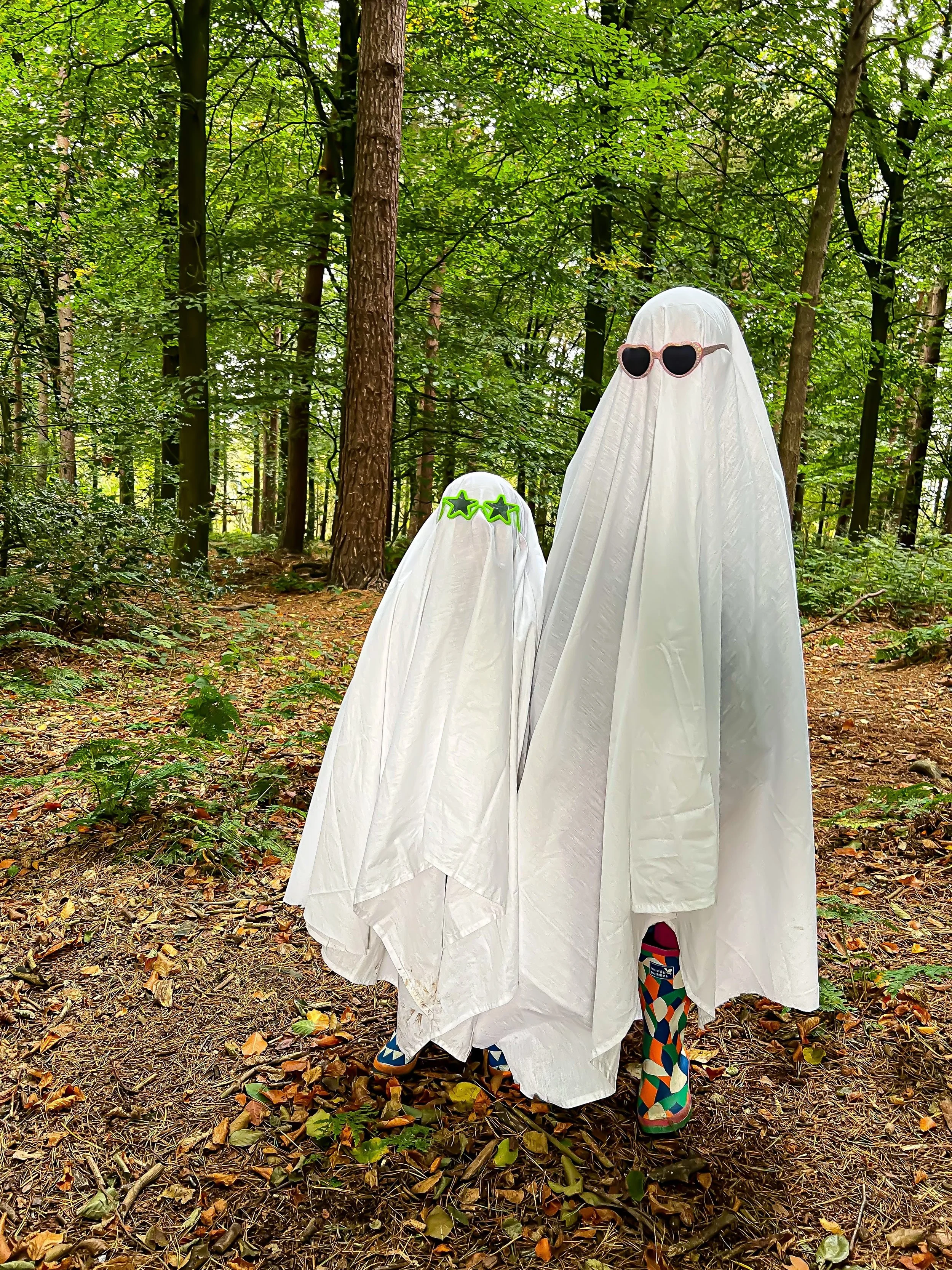 Children dressed as a ghost in white sheets with sunglasses on in the woods