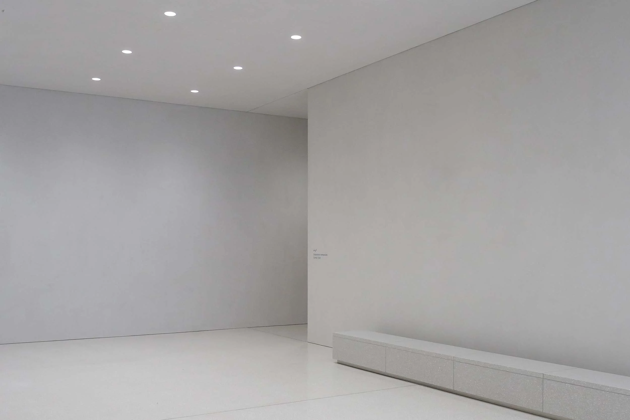 Minimalist gallery space with light marble walls, seamless marble flooring, and an integrated marble bench