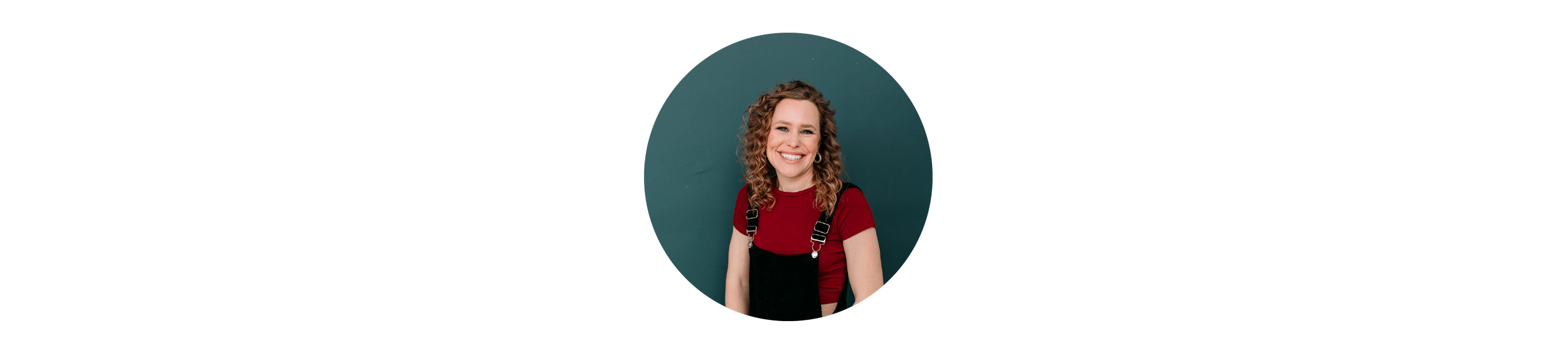 A young woman with curly hair wearing a red shirt and black overalls, smiling against a teal background.
