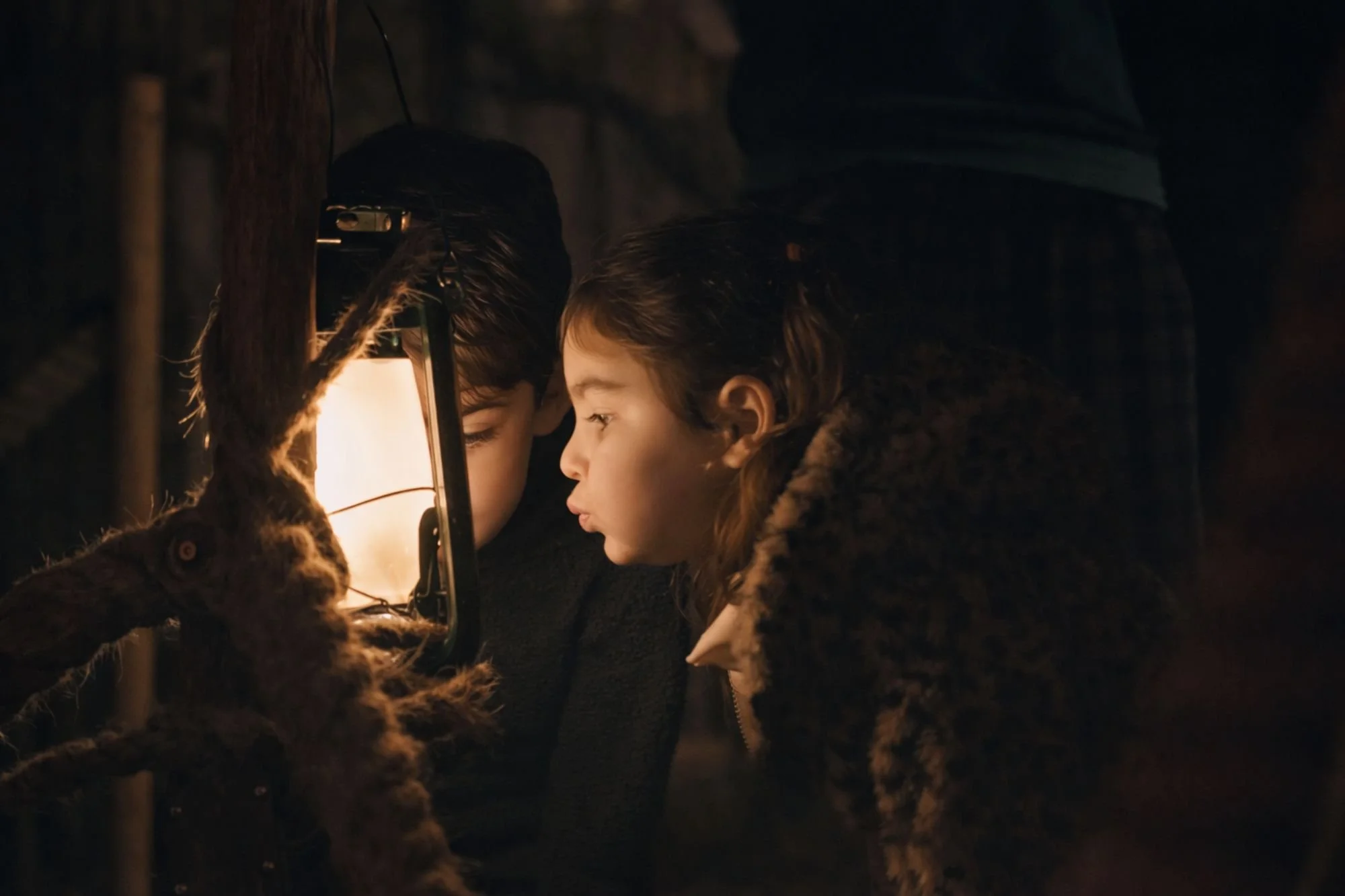 A young boy and girl in the forest near a lamp reading