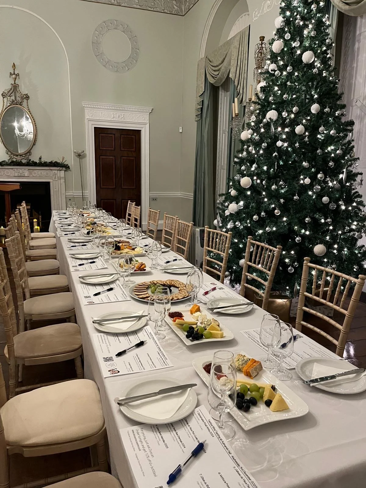 Wine glasses and cheese and fruit platters on a dining table with a Christmas tree next to it