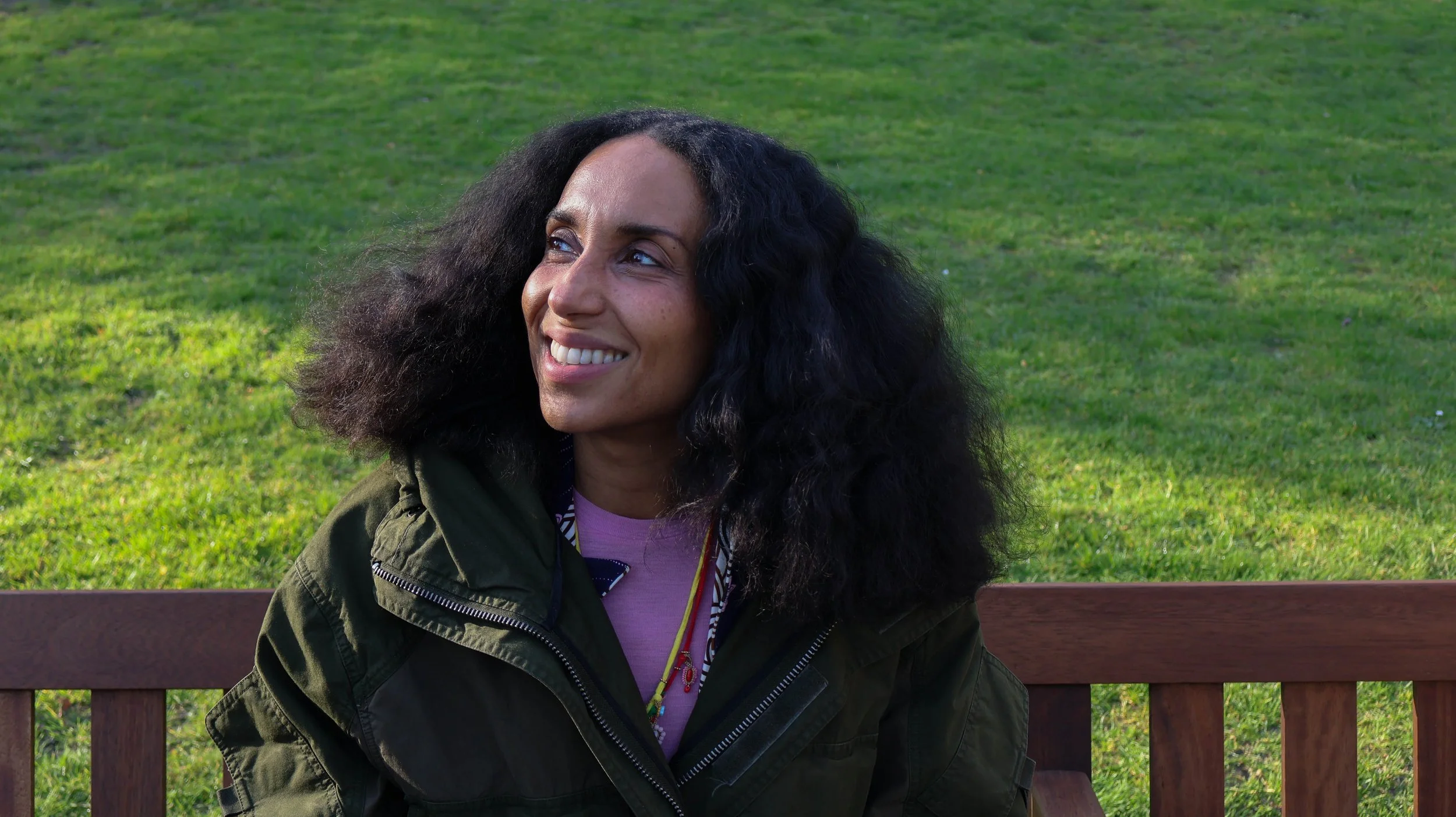 Chioma Nnadi, Head of Editorial Content of British Vogue, smiling on a bench in Embankment Gardens 