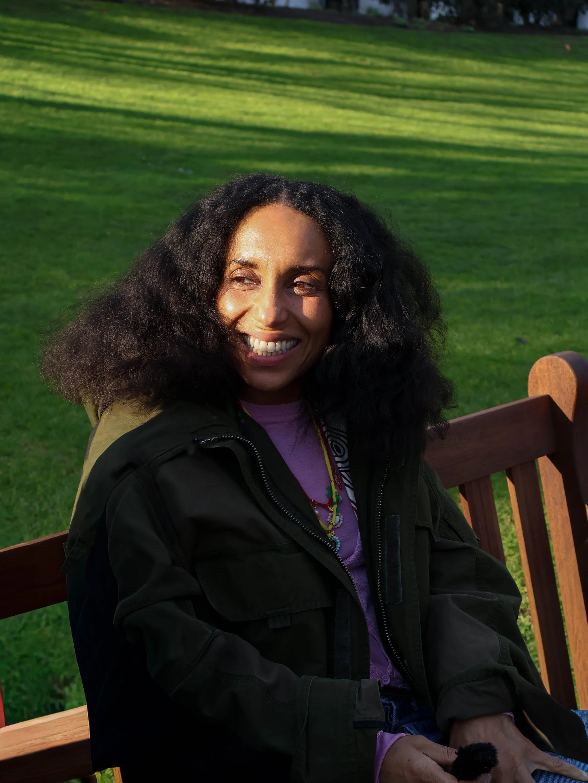 Chioma Nnadi, Head of Editorial Content of British Vogue, smiling on a bench in Embankment Gardens 