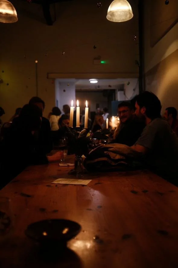 Dimly lit restaurant scene with candles on a wooden table and people dining