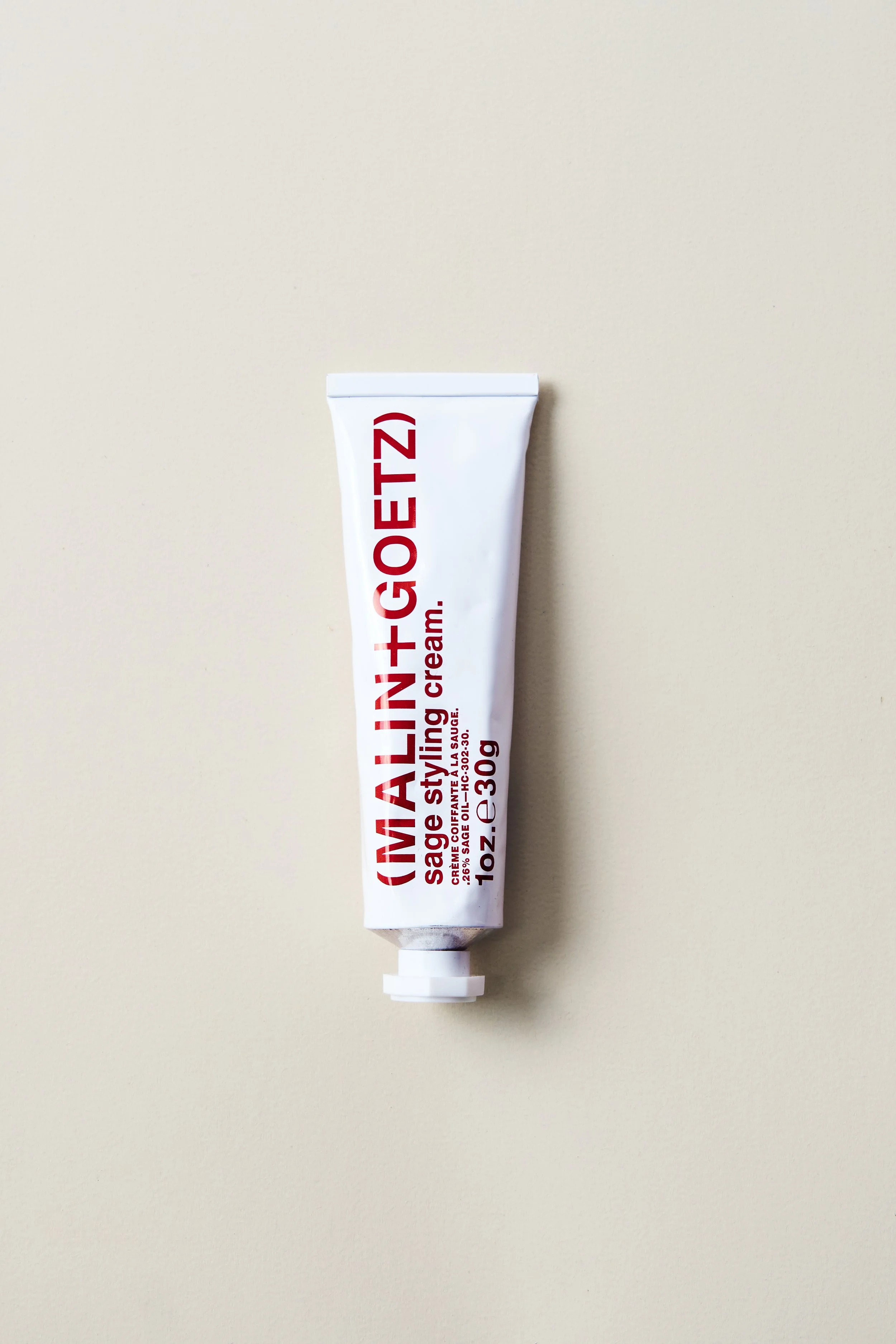 A tube of Malin+ Goetz sage styling cream on a plain light-colored background.