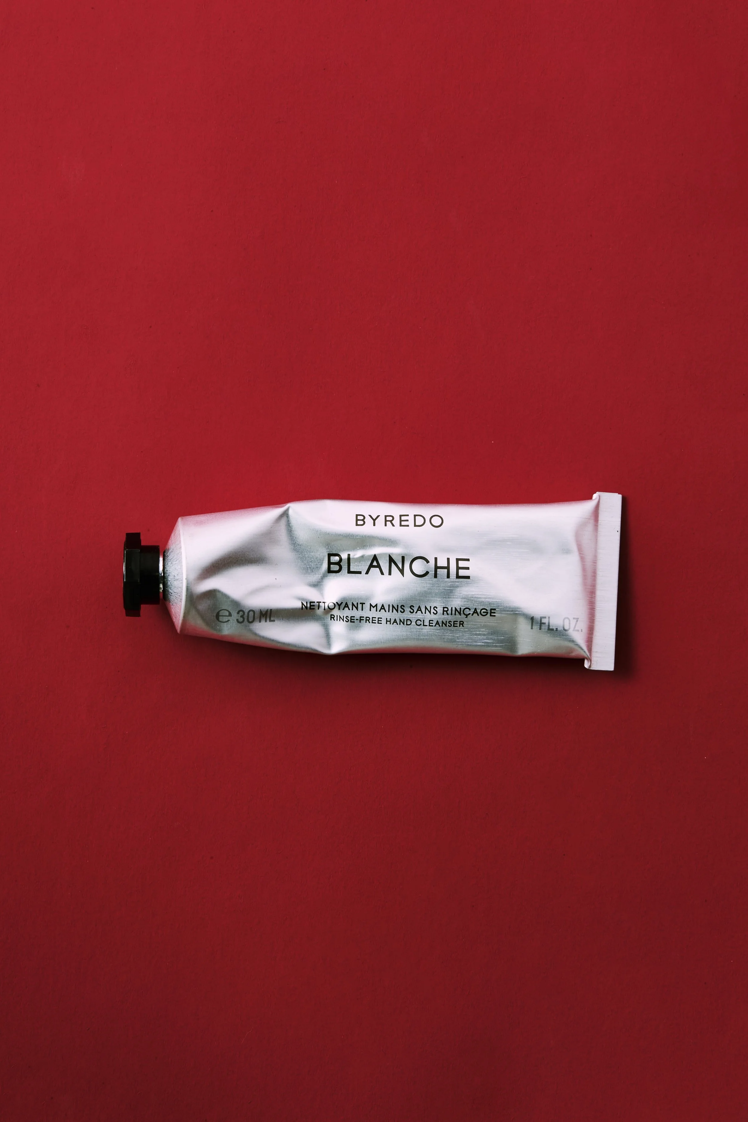 A silver tube of BYREDO Blanche rinse-free hand cleanser on a red surface.
