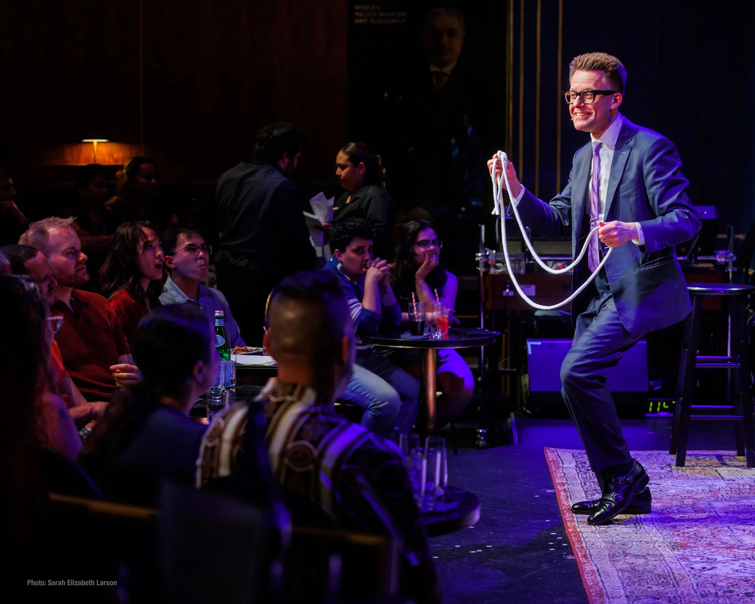 Arthur Trace performs a rope trick on stage while an audience watches and reacts with excitement.