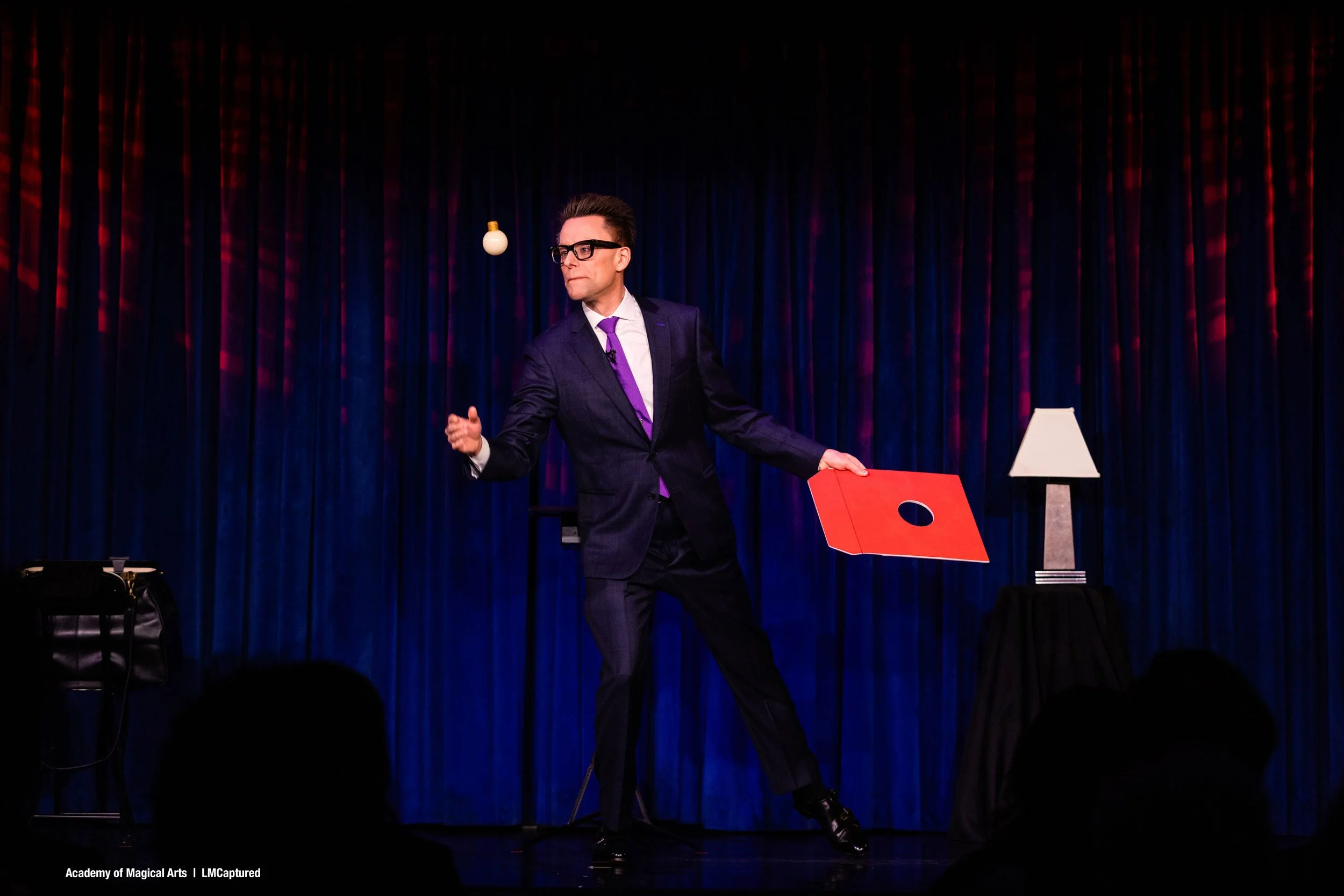 Arthur Trace, midperformance, throws a lightbulb into the air. He holds a record sleeve in his other hand.
