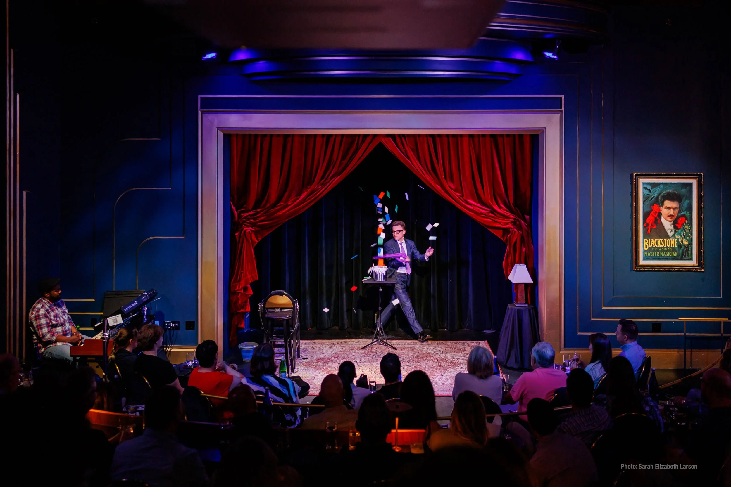 Arthur Trace performing on stage. The photo captures the finale of his act where colored cards are shooting up into the air from a paint bucket.