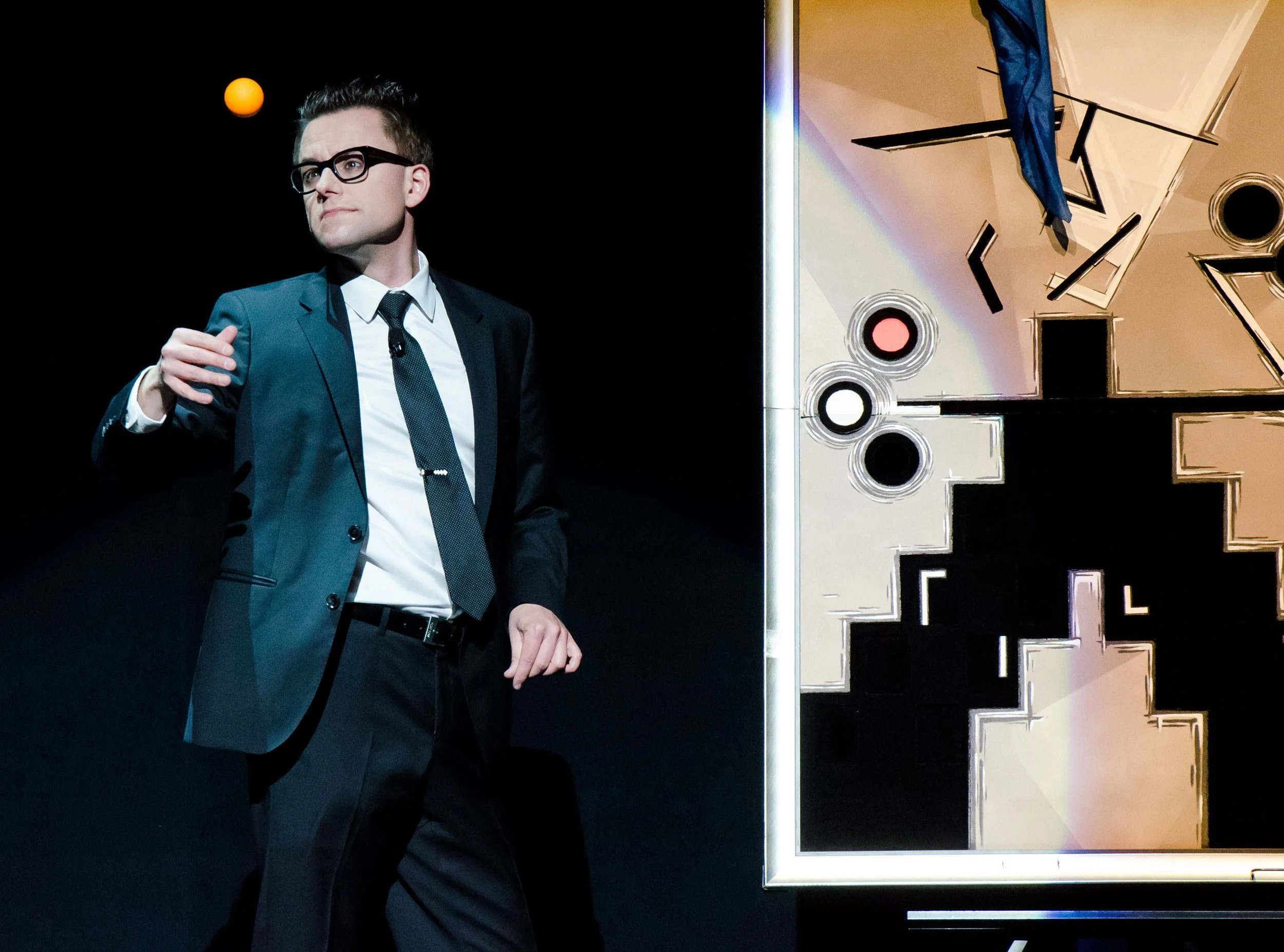 Arthur Trace performs his Postmodern Art act. The photo captures a moment of sleight of hand with a ball and an abstract painting is visible in the background.