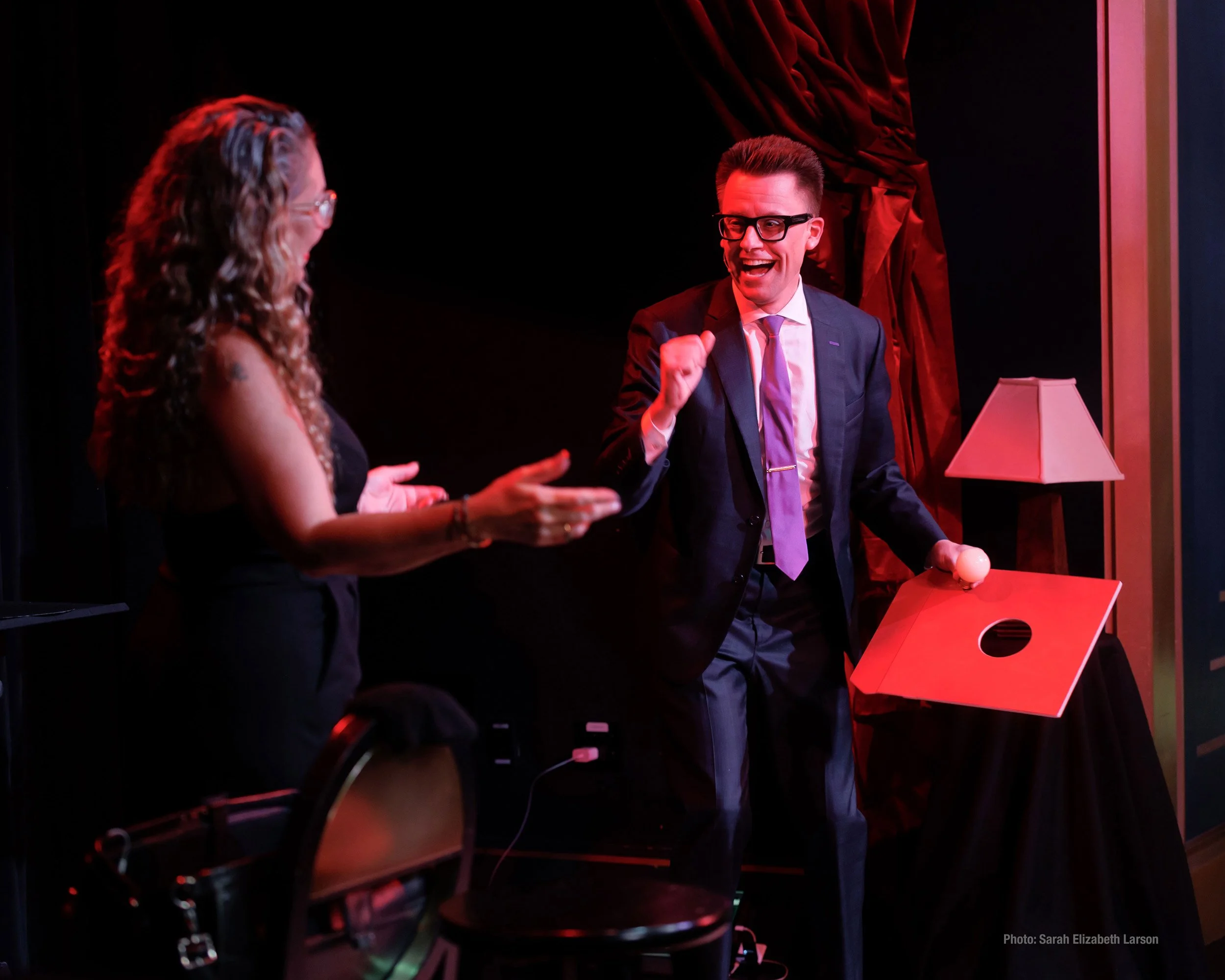 Arthur Trace and female volunteer are on stage at The Chicago Magic Lounge. Arthur is smiling and addressing her.