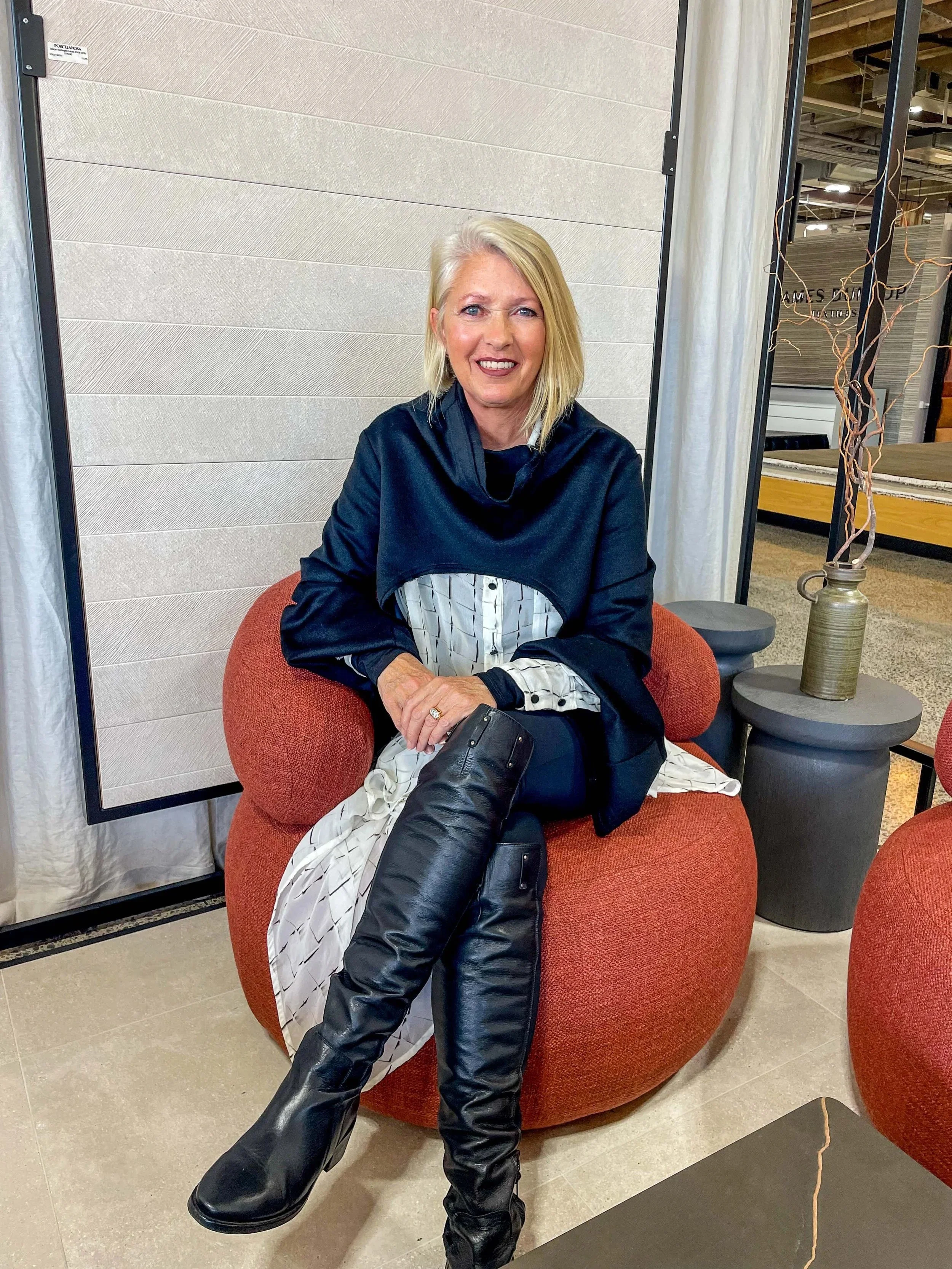 Interior Designer - Lianne McMahon or McMahon Design based in Auckland and servicing Auckland North Shore, Auckland City Center, East and West Auckland. Lianne is sitting in an interiors show room on an orange swivel chair.