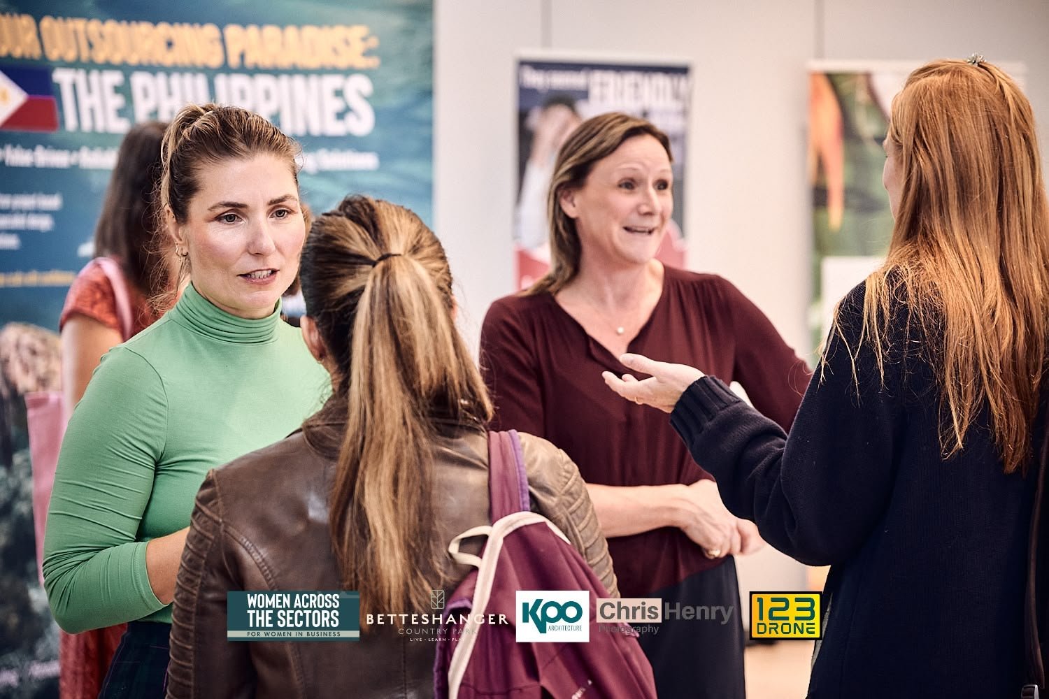 Four women engaged in conversation at an indoor event, with banners and posters in the background about women in business and travel in the Philippines.