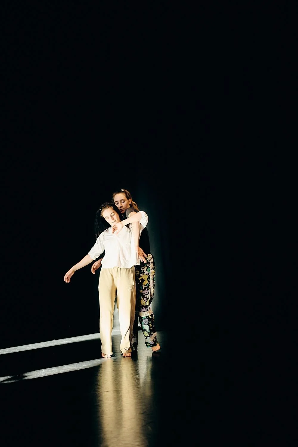 Two women are dancing on a dark stage with minimal lighting, creating a dramatic atmosphere.