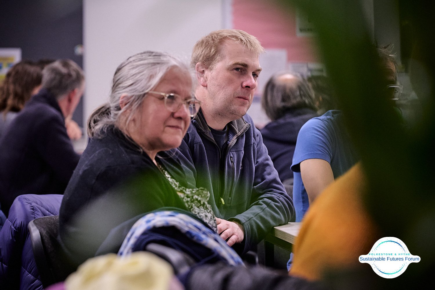 A group of people sitting at a conference table listening attentively, with a logo for the 'Sustainable Futures Forum' in the bottom right corner.