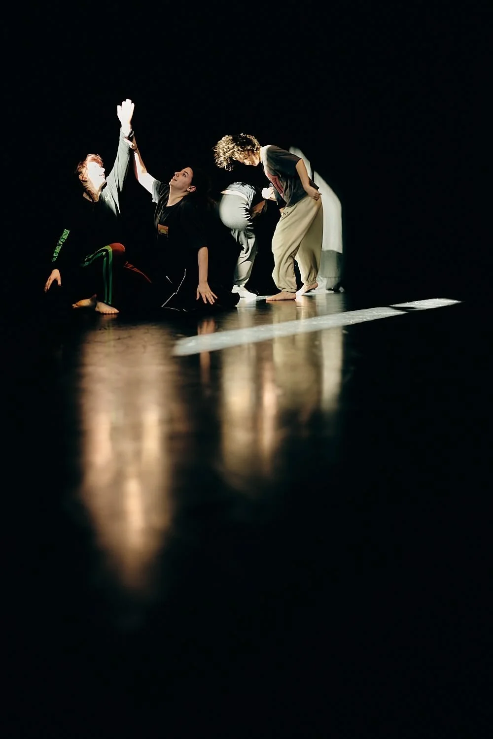 Four people performing a dance or theatrical act on stage in a dark setting with spotlight, engaged in expressive poses.