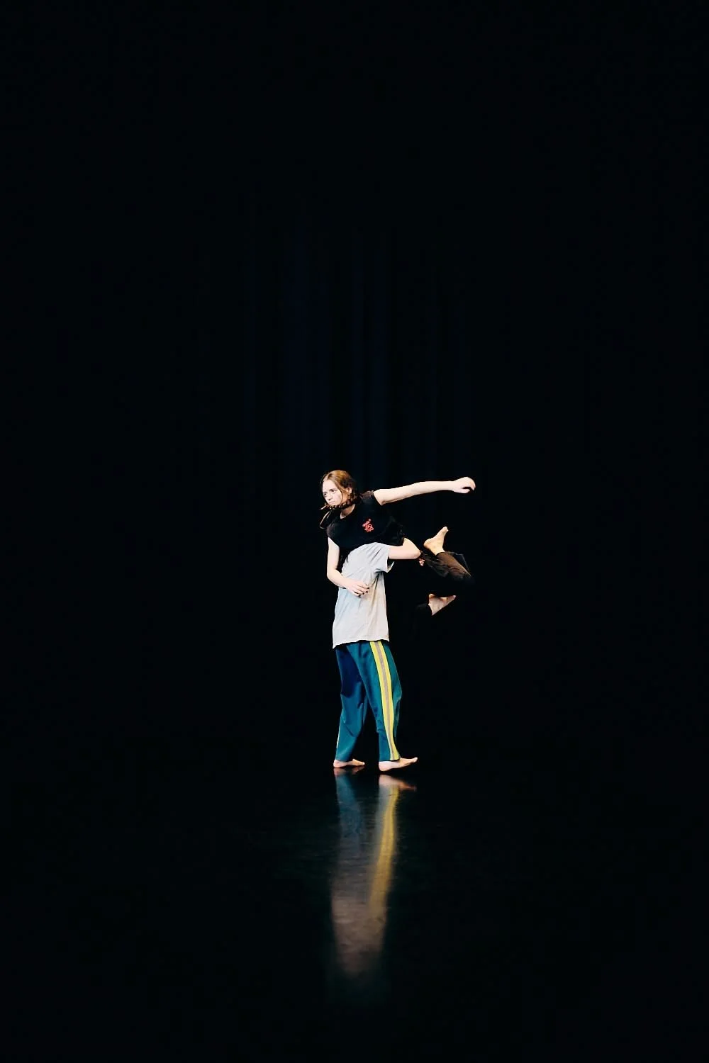 Two performers dancing on a dark stage, one is lifting the other who is in mid-air