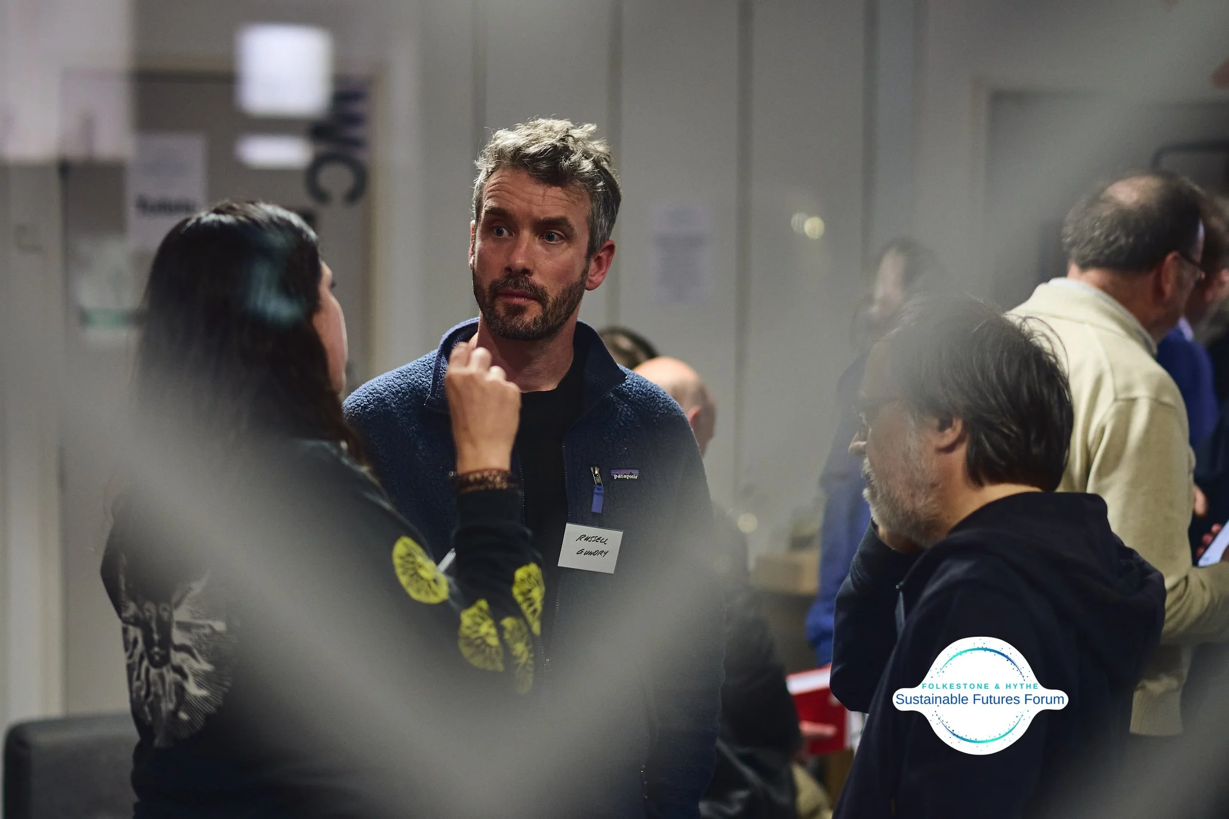 People talking and networking at the Sustainable Futures Forum, with a focus on three individuals in the foreground engaged in conversation.