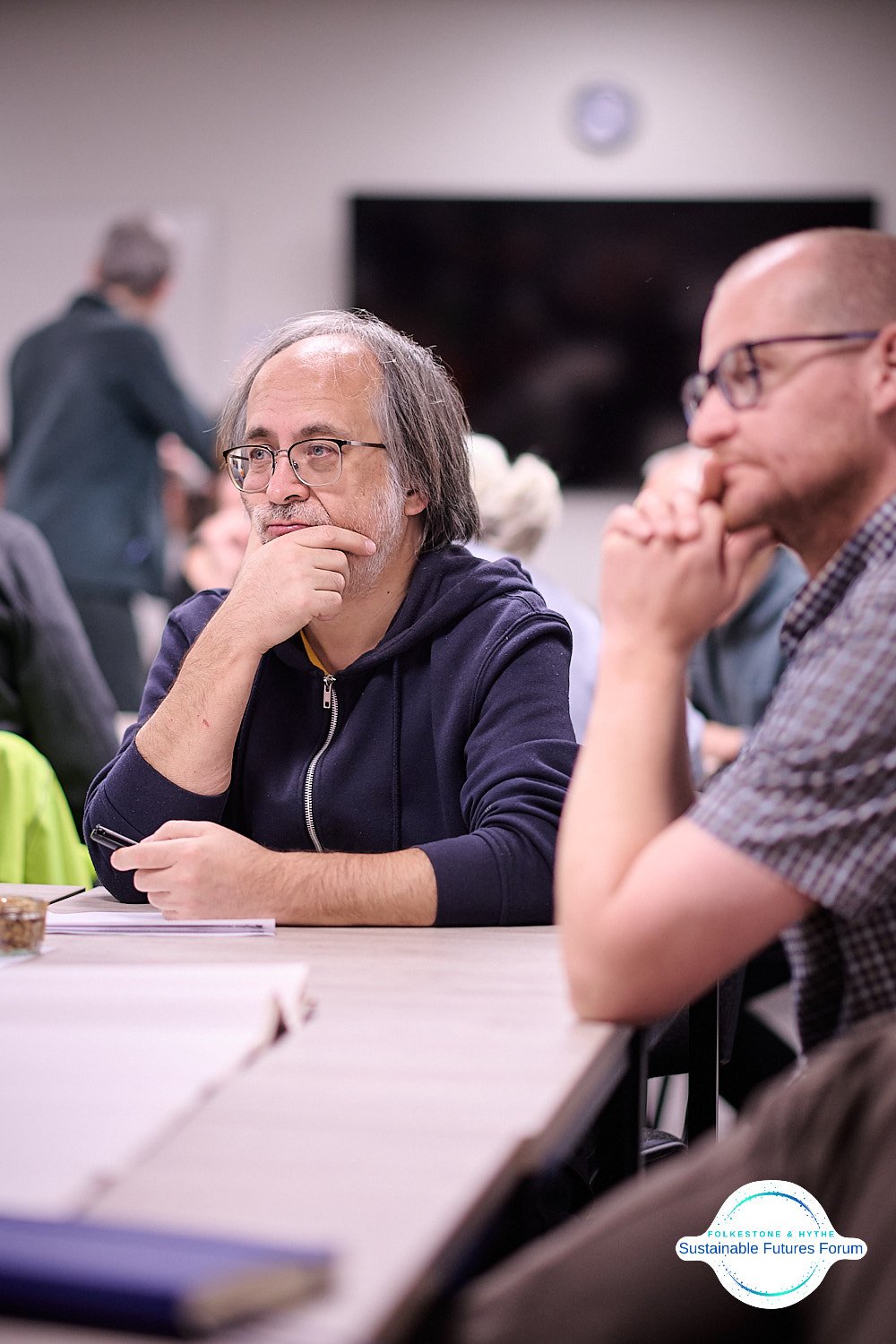 Two men sitting at a table, deep in thought, attending a meeting at the 'Folkes Tone & Thyne Sustainable Futures Forum'.
