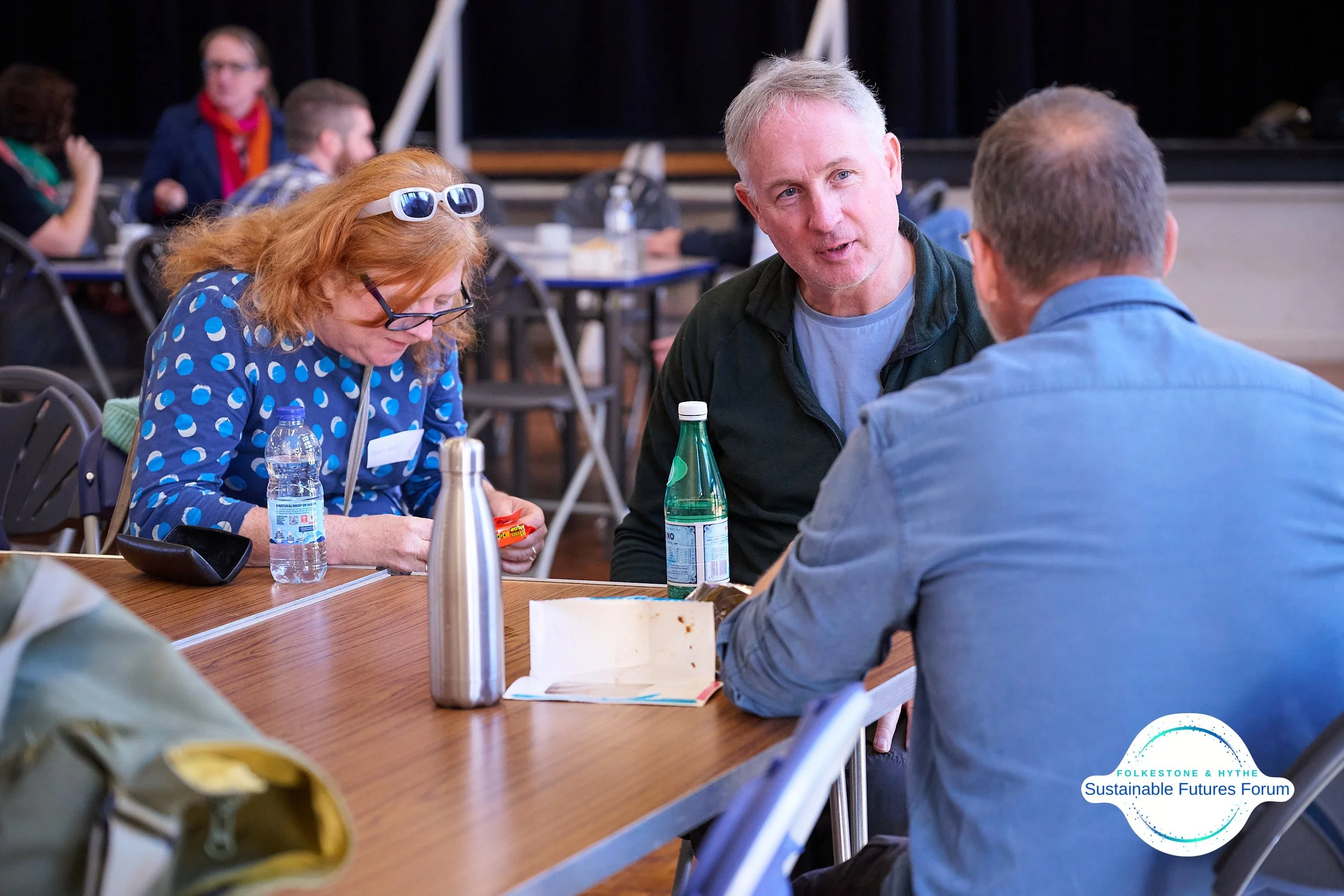 Three people engaged in conversation at a conference table during the Folkestone & Hythe Sustainable Futures Forum.