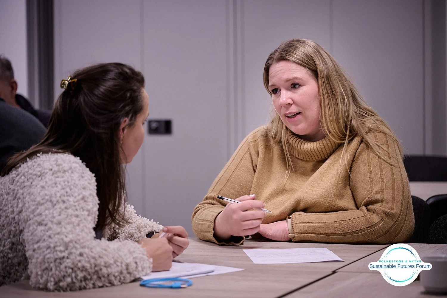 Two women engaged in conversation at a table, discussing documents, at the Sustainable Futures Forum event.