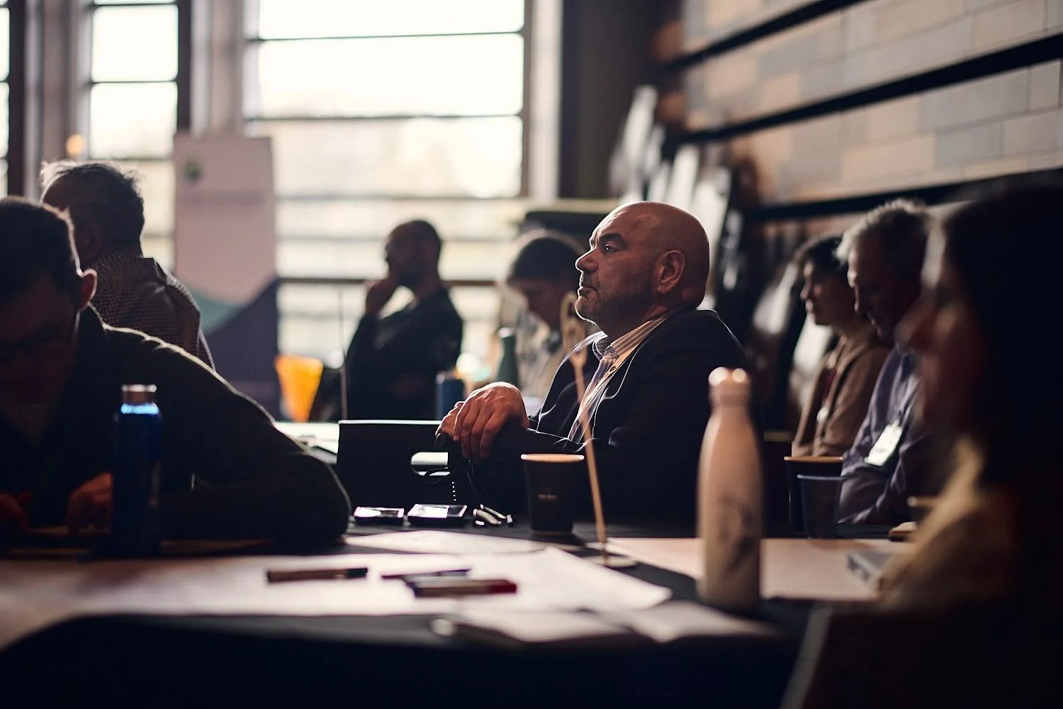 Man listening to conference presentation surrounded by colleagues