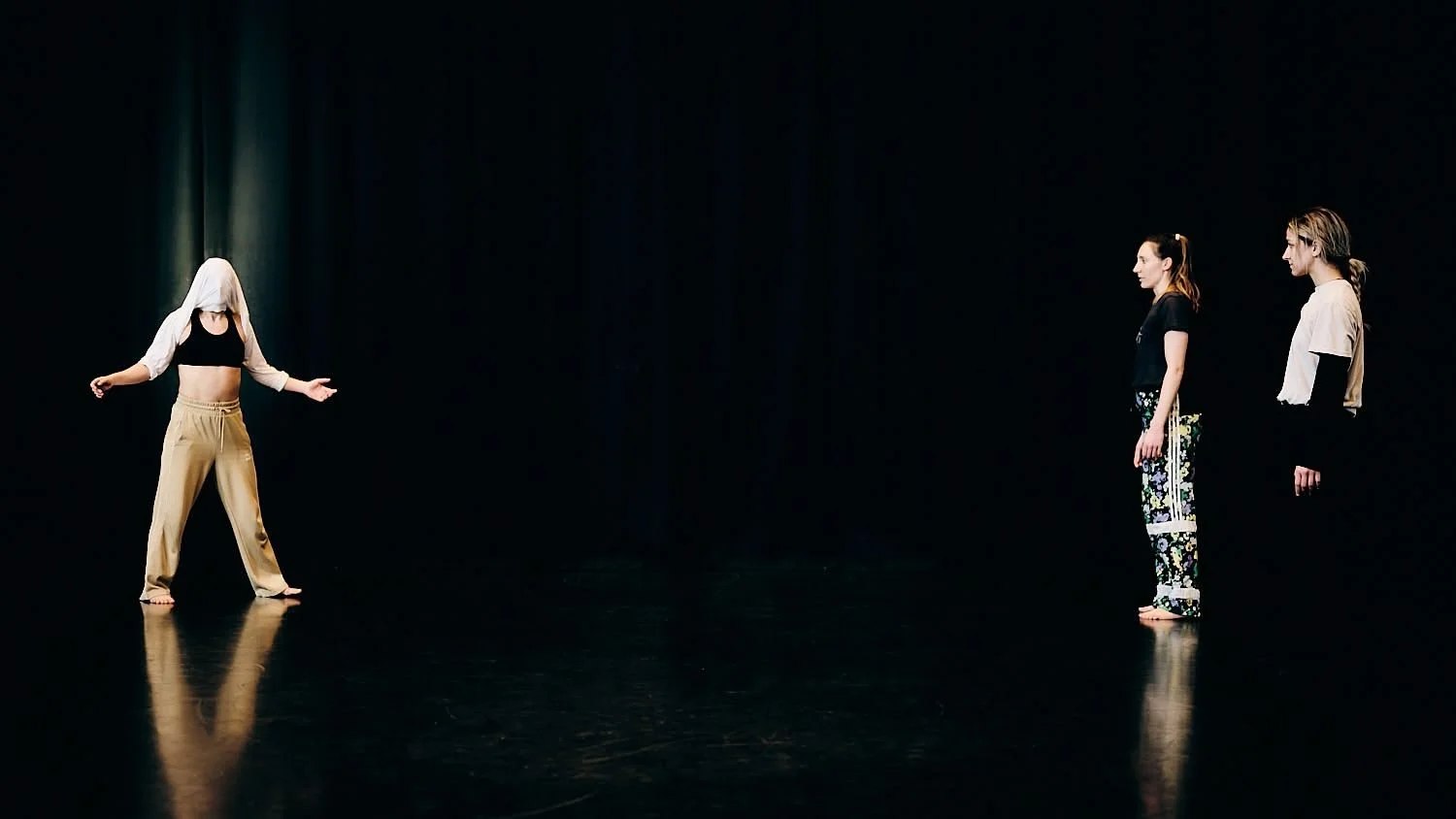 Four women standing in a dark space, one with a hood over her head, facing three others in a line.