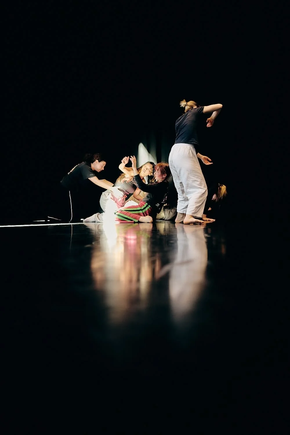 Group of women practicing or rehearsing a dance or theater performance on a dark stage.