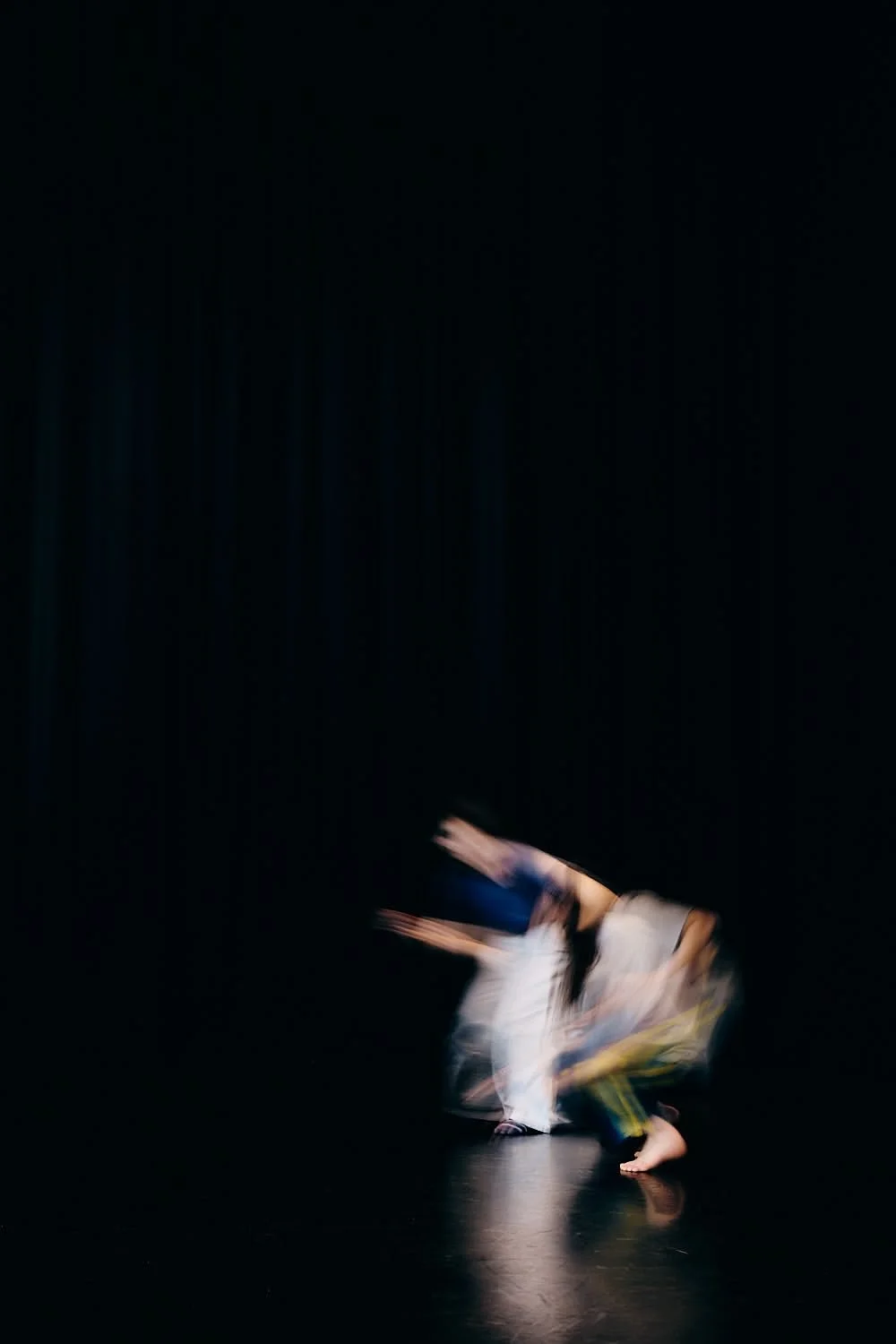 Two dancers performing on a dark stage with a black background.