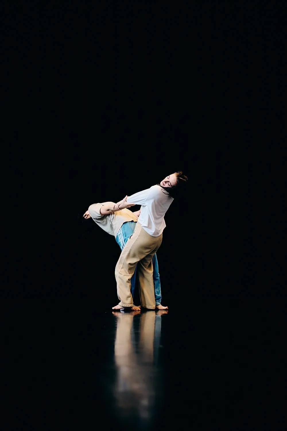 Two dancers perform on a dark stage, with one dancer bent backward supported by the other.