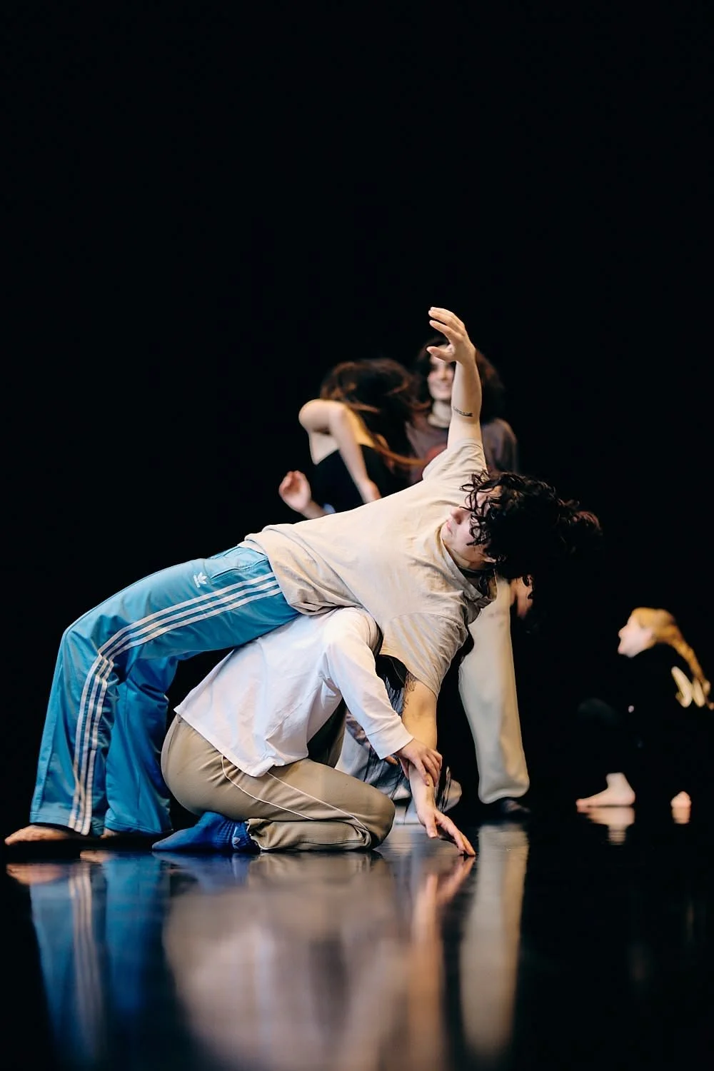 Multiple dancers performing in a contemporary dance pose on stage with a black background.