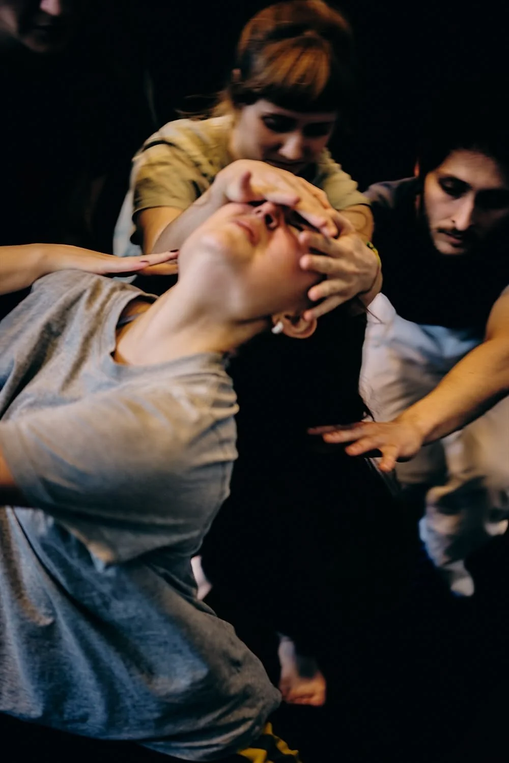 Individuals engaged in a dramatic scene, with one person clutching their face and being supported by others in a dark setting.