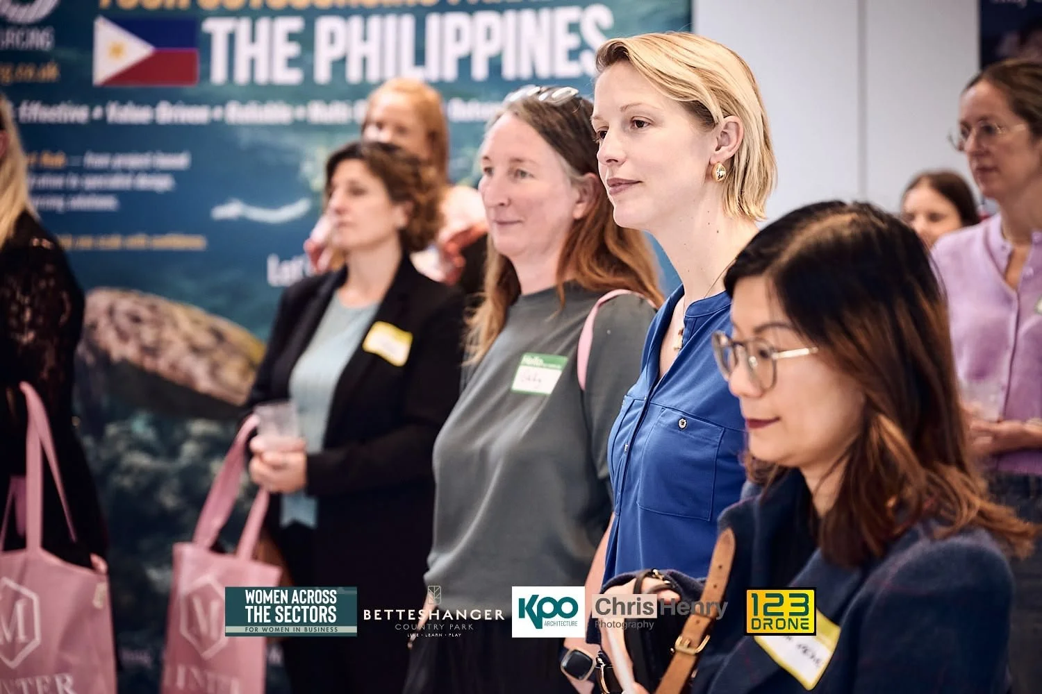 Group of women attending the Women Across the Sectors event in front of a large banner displaying a Philippine flag and scenic background.