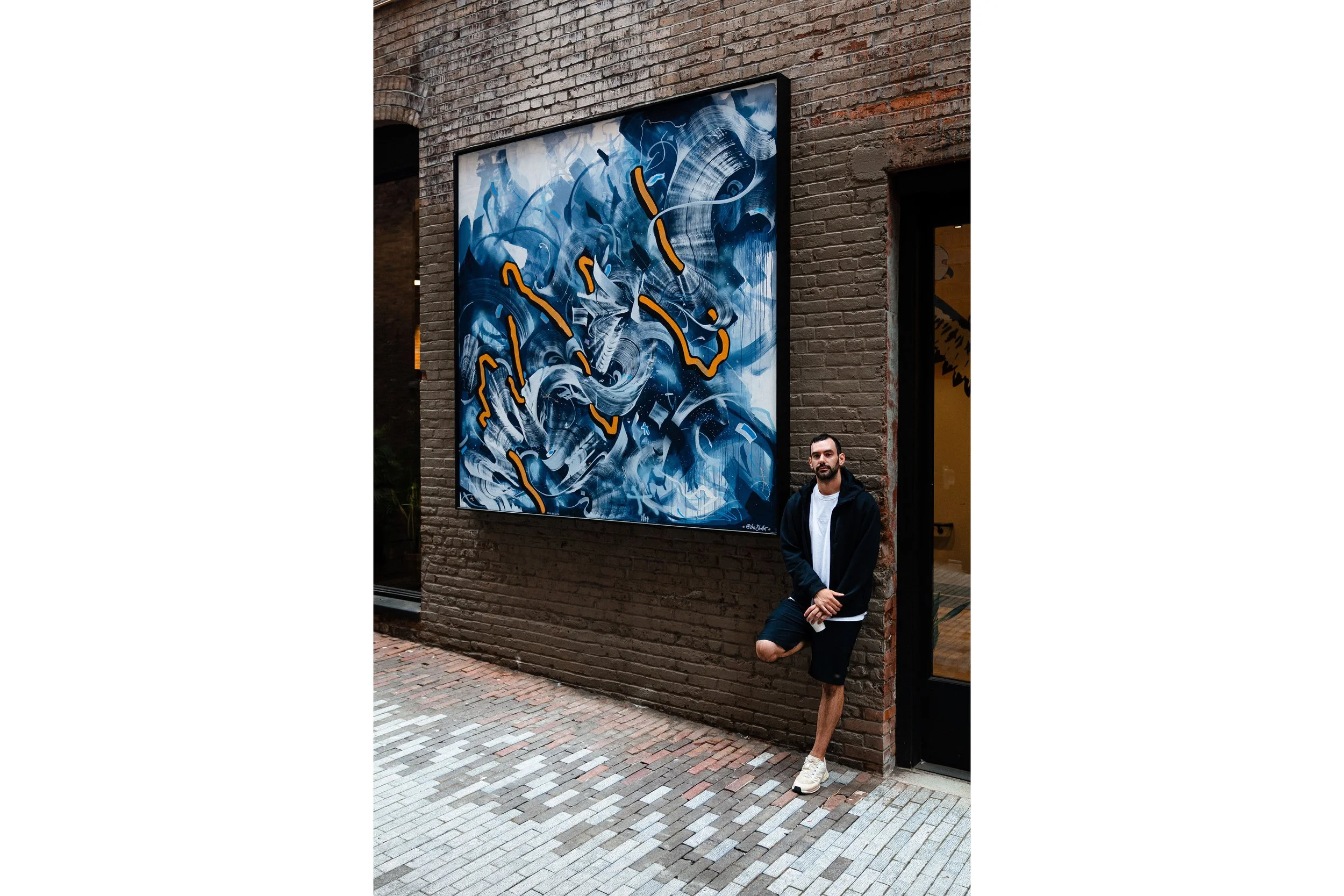 A man stands beside a large abstract mural on brick wall