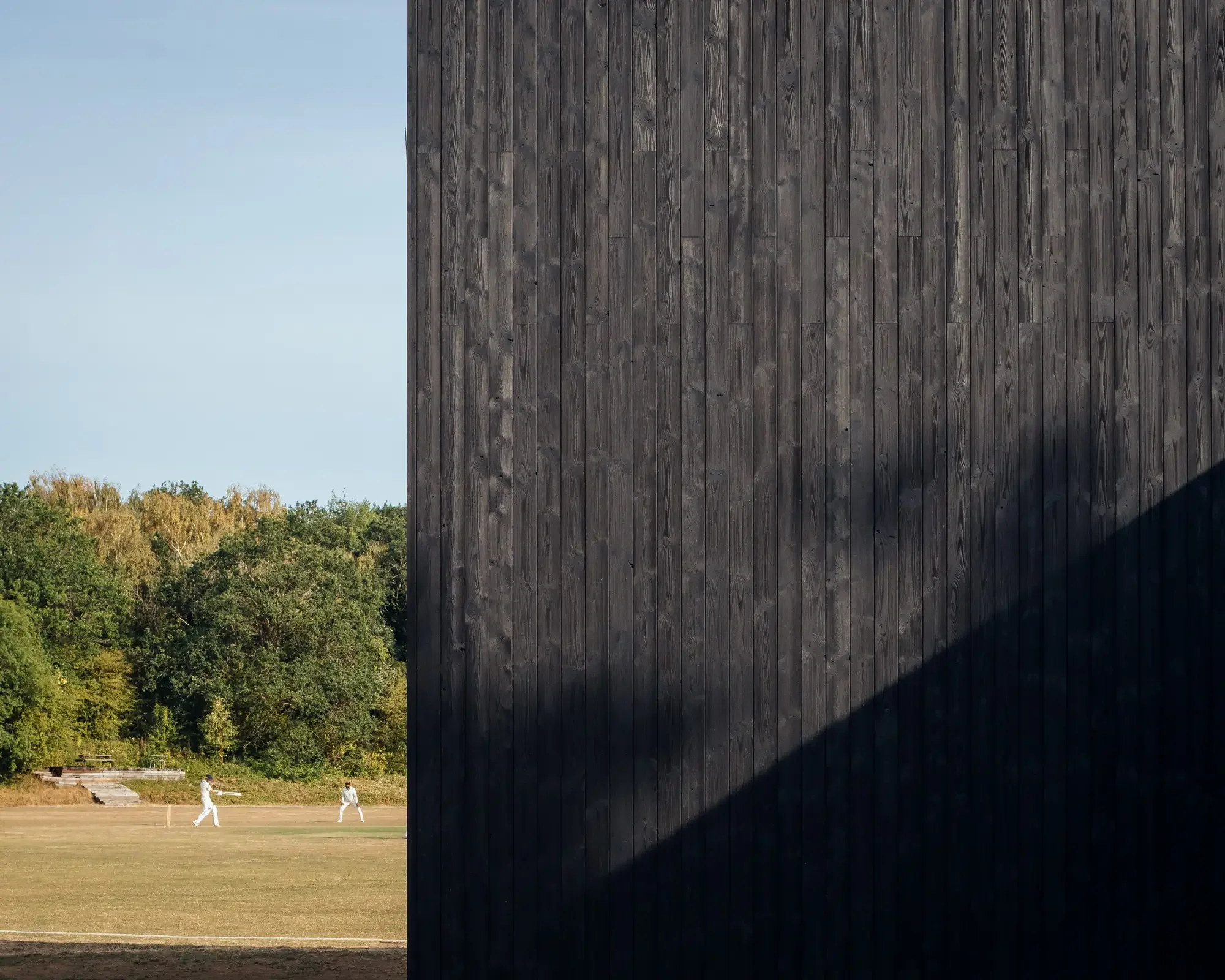 Shou Sugi Ban timber cladding with cricket game in the background © Jim Stephenson