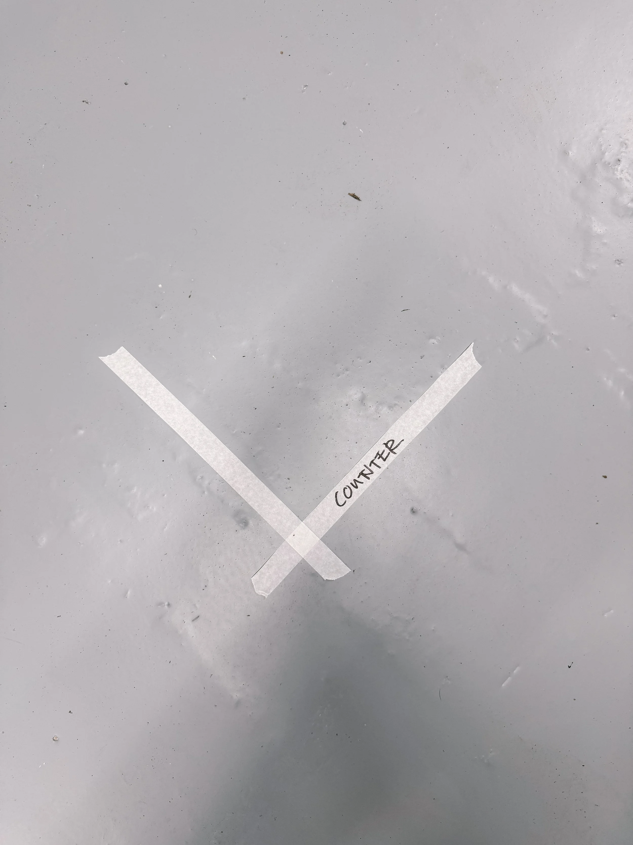 A white surface with a piece of tape forming a checkmark shape and the word 'Counter' written on one part of the tape.
