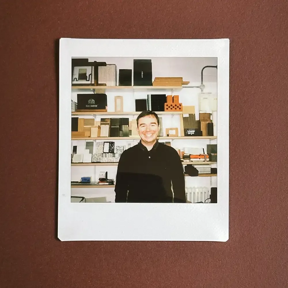 A man shown in a Polaroid style image laid on dark red table.