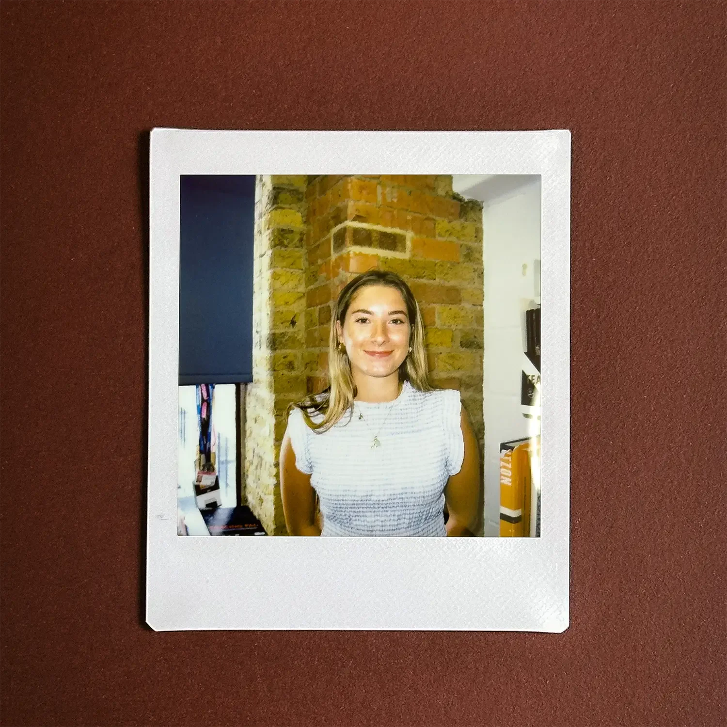 A young woman shown in a Polaroid style image laid on dark red table.