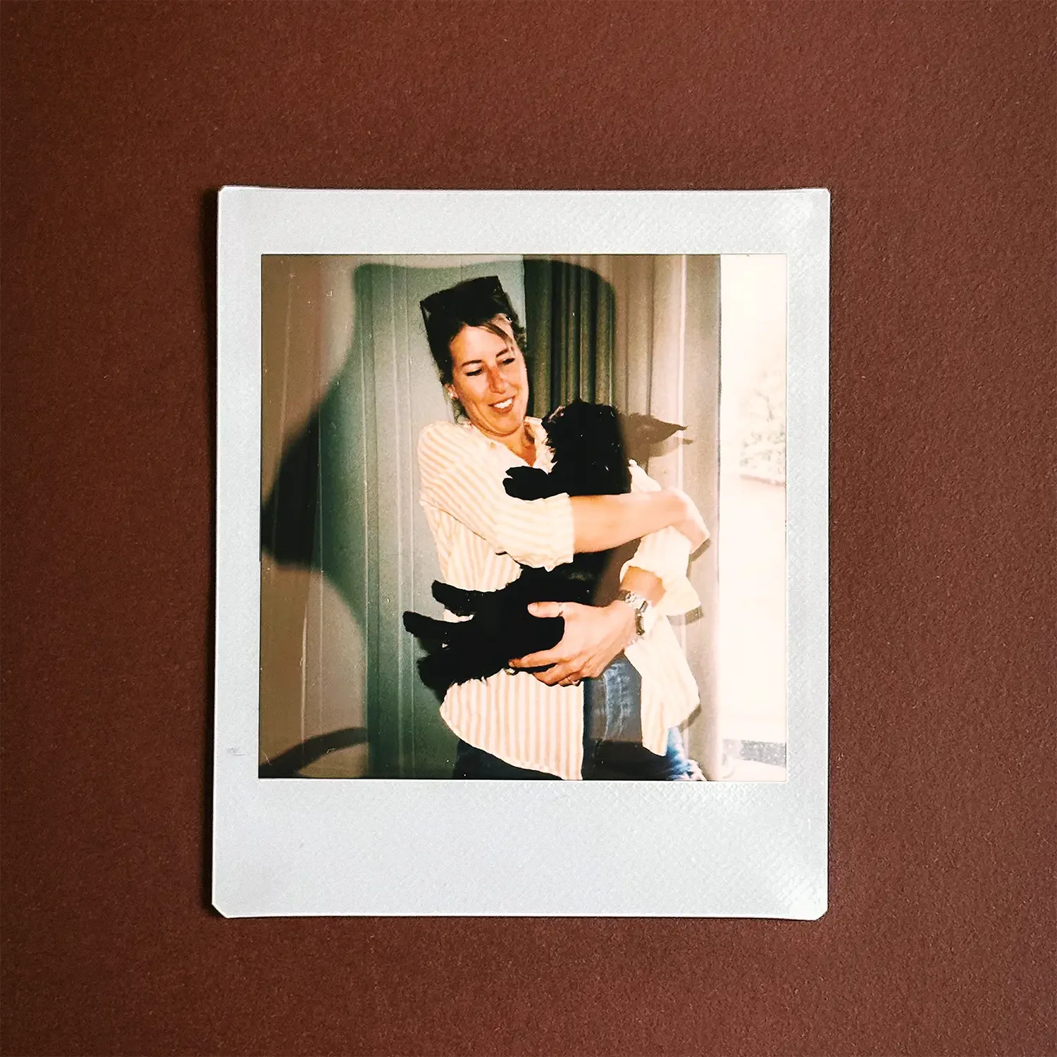 A woman and black scruffy dog shown in a Polaroid style image laid on dark red table.