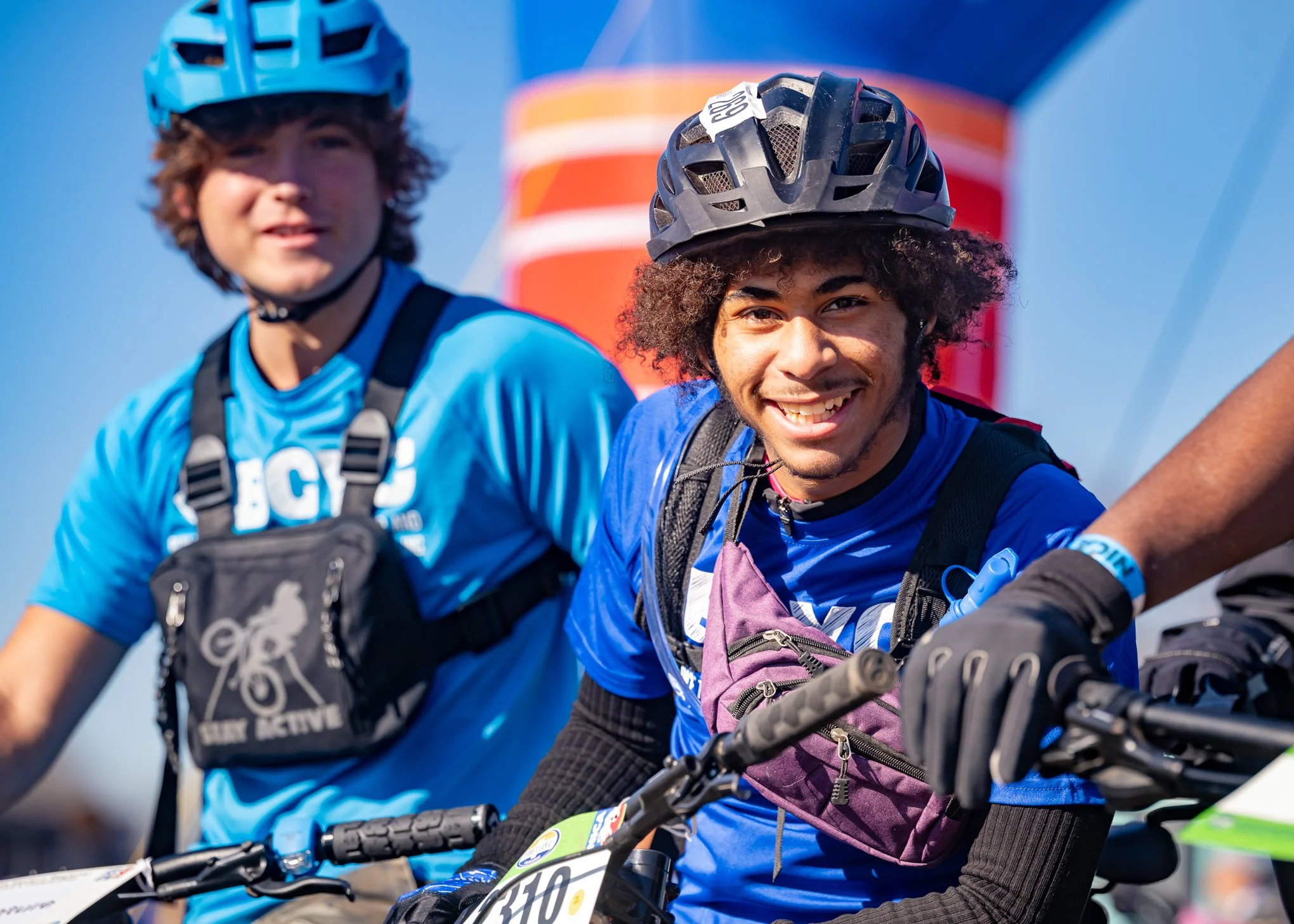 Two young men wearing blue shirts and helmets riding bicycles outdoors during daytime.